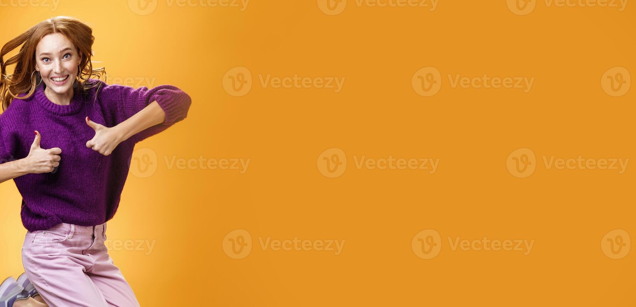 Optimistic and cheerful woman liking promotion lifting thumbs up and jumping from excitement and delighted, having fun recommending good idea smiling thrilled and enthusiastic over orange background photo