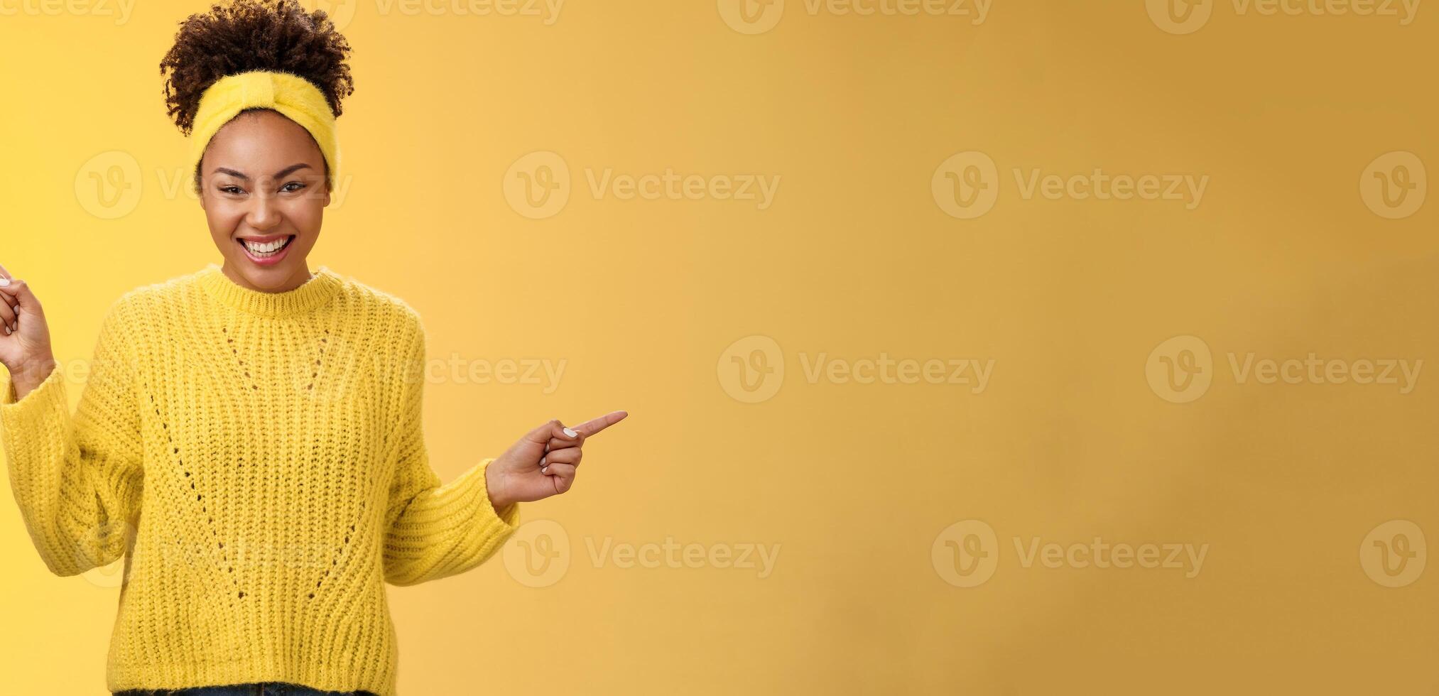 Charming tender romantic young african-american 20s woman smiling friendly satisfied laughing lovely look camera pointing up right sideways show products choices two ways, standing yellow background photo