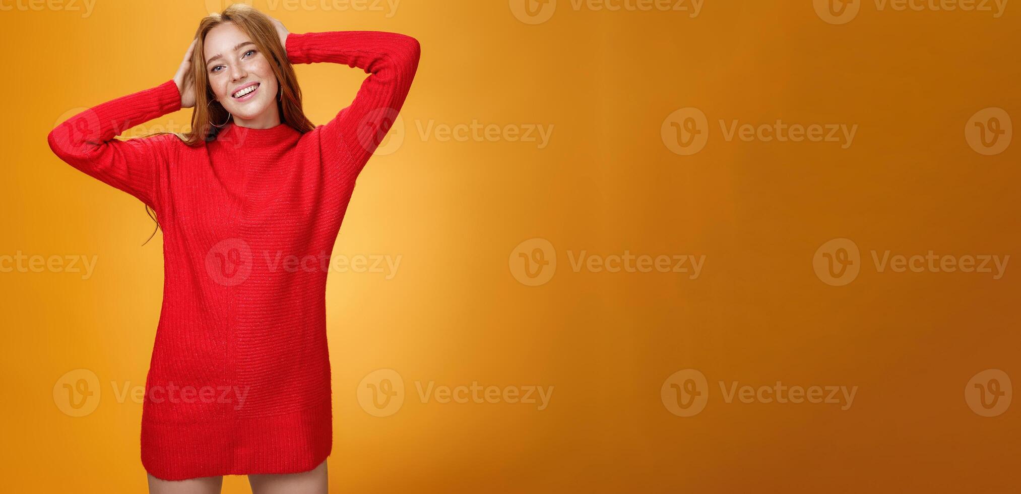 Romantic and sensual cute ginger girlfriend in elegant warm red winter dress holding hands behind head relaxed and carefree smiling delighted tilting head enjoying leisure and holidays photo