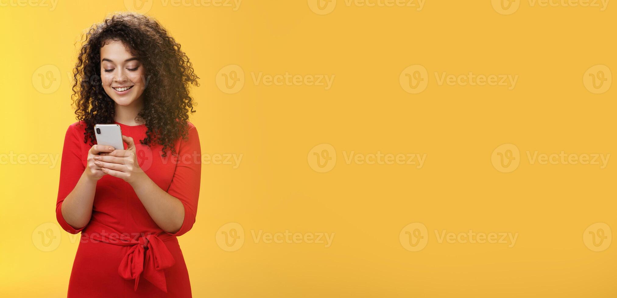 Gil sending message spread news across social network having party inviting friends via smartphone holding mobile phone in hands smiling broadly at device screen as posing over yellow background photo