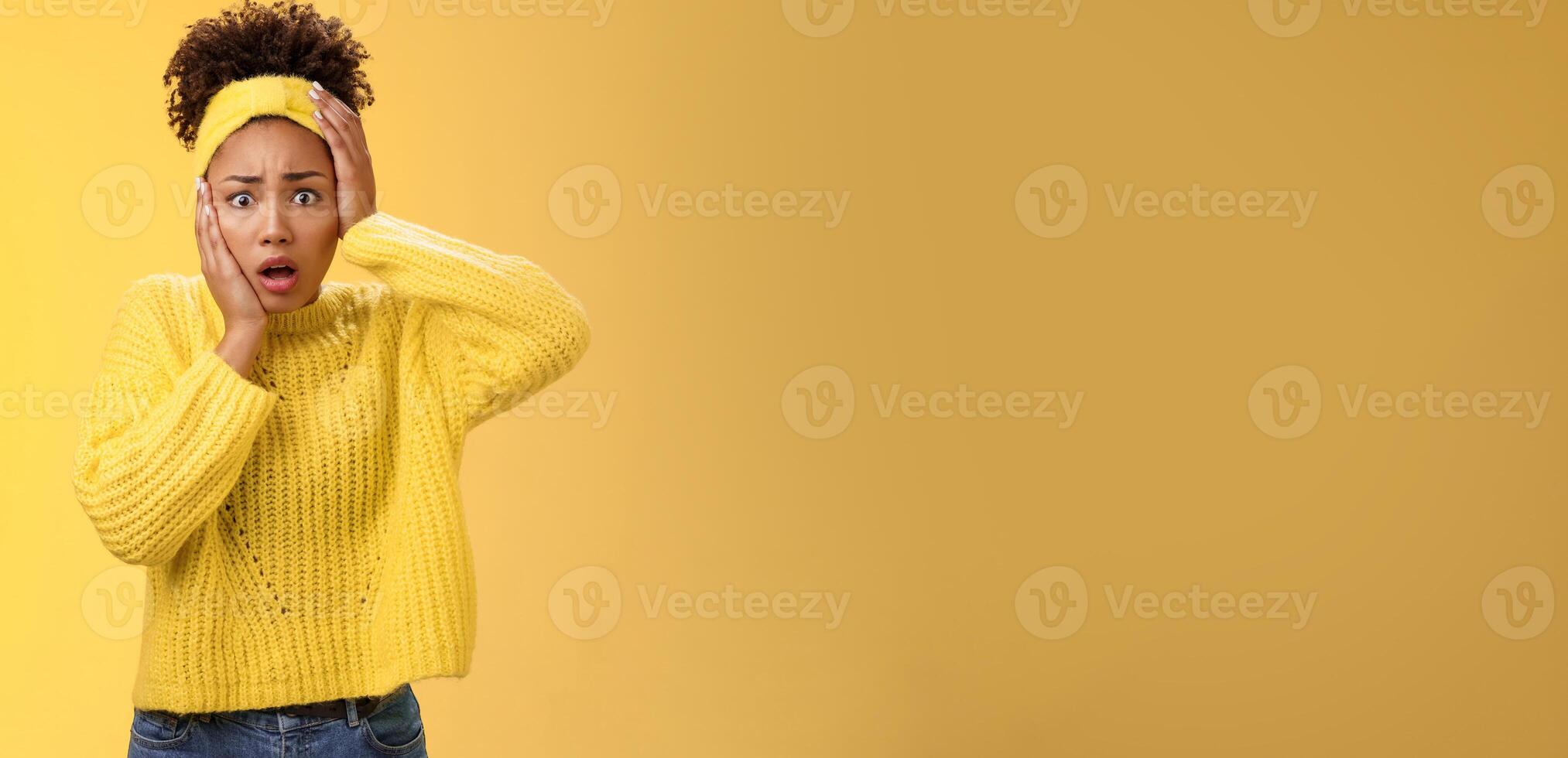 Shocked terrified timid insecure young stylish african-american woman panic touch face concerned gasping open mouth widen eyes frightened bad consequences standing upset nervous yellow background photo