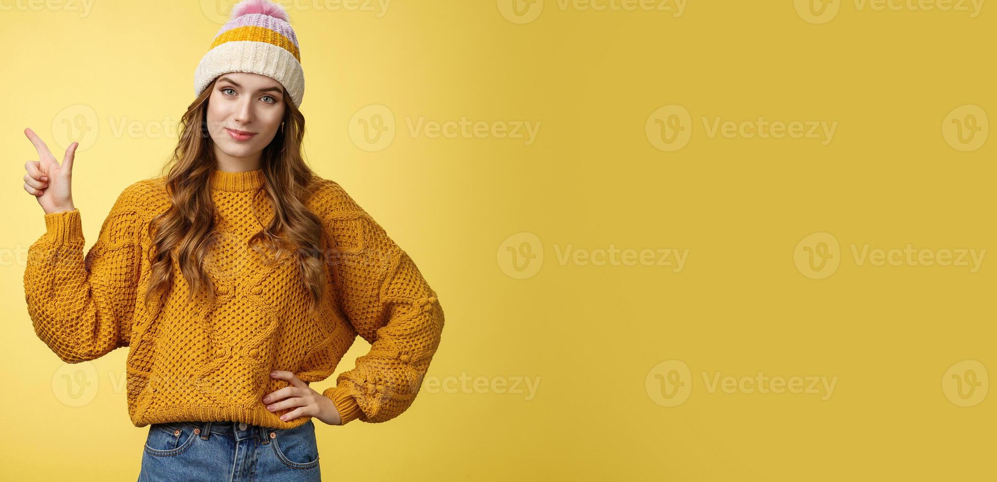 Confident good-looking young female friend telling you buy product immidietely pointing upper left corner smiling hold hand waist self-assured, employee help client pick best merch, yellow background photo