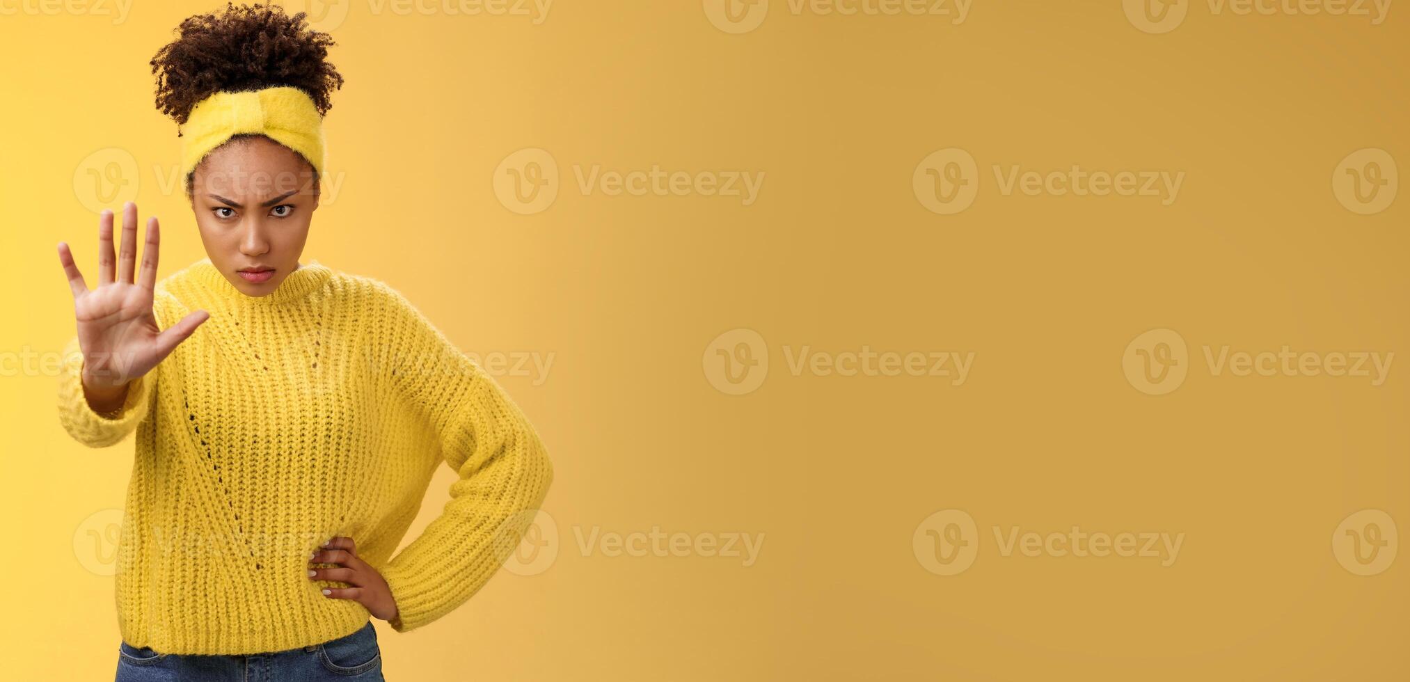 Brave serious-looking female african american femenist look from under forehead confident powerful pose raise palm stop enough not decline gesture forbid behave bad, standing yellow background photo