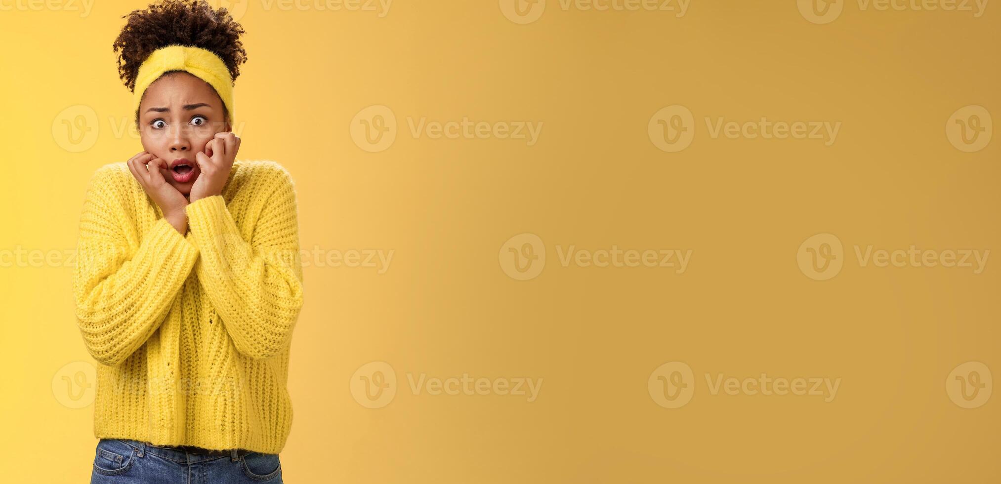 Scared stupefied trembling insecure timid african american woman afraid widen eyes gasping touching face terrified look horror eyes terrified cannot move shaking fear, standing yellow background photo