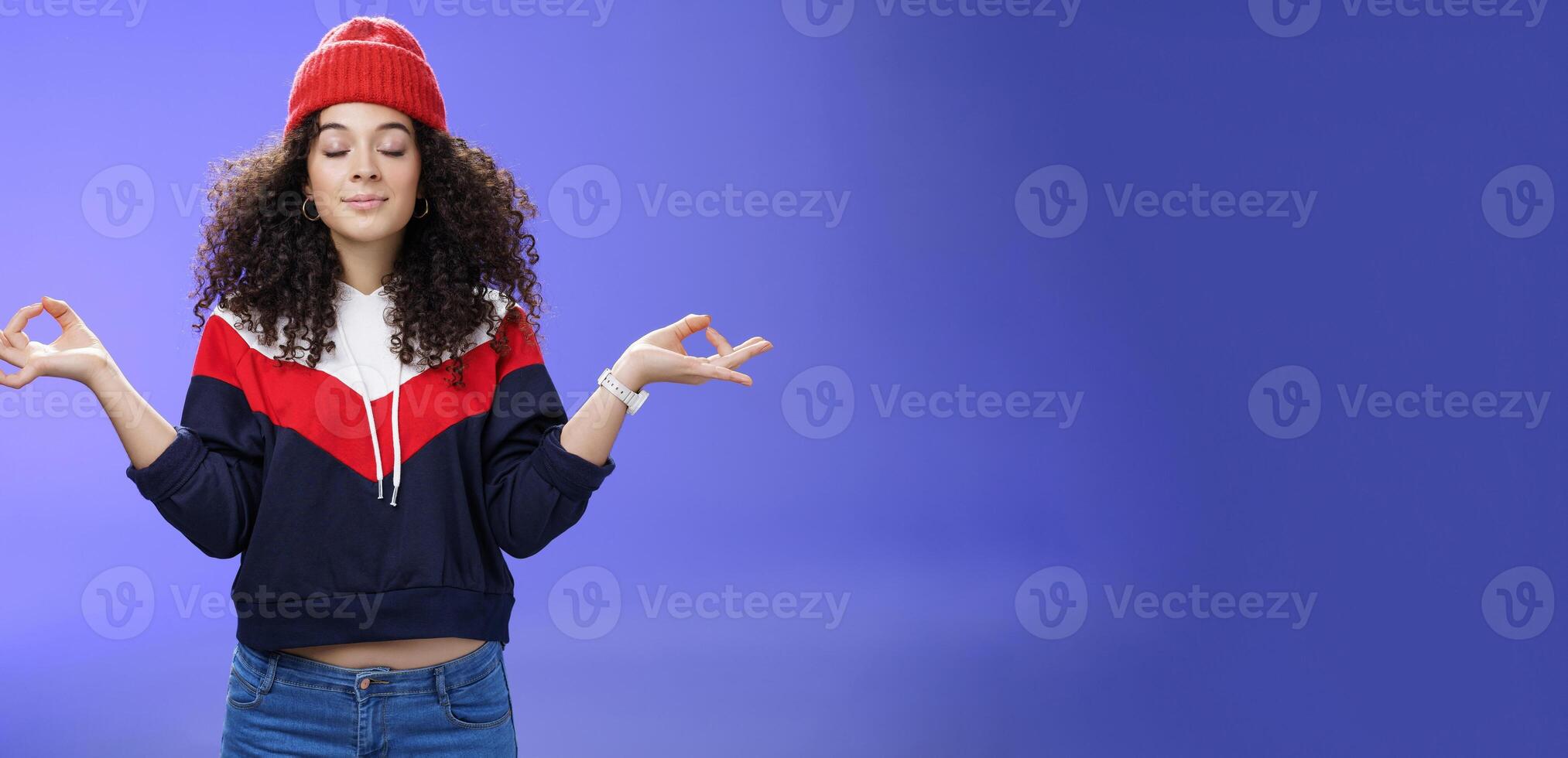 Waist-up shot of girl reaching nirvana feeling peaceful and calm holding hands sideways with mudra gesture close eyes, meditating releasing stress standing calm in lotus pose over blue background photo