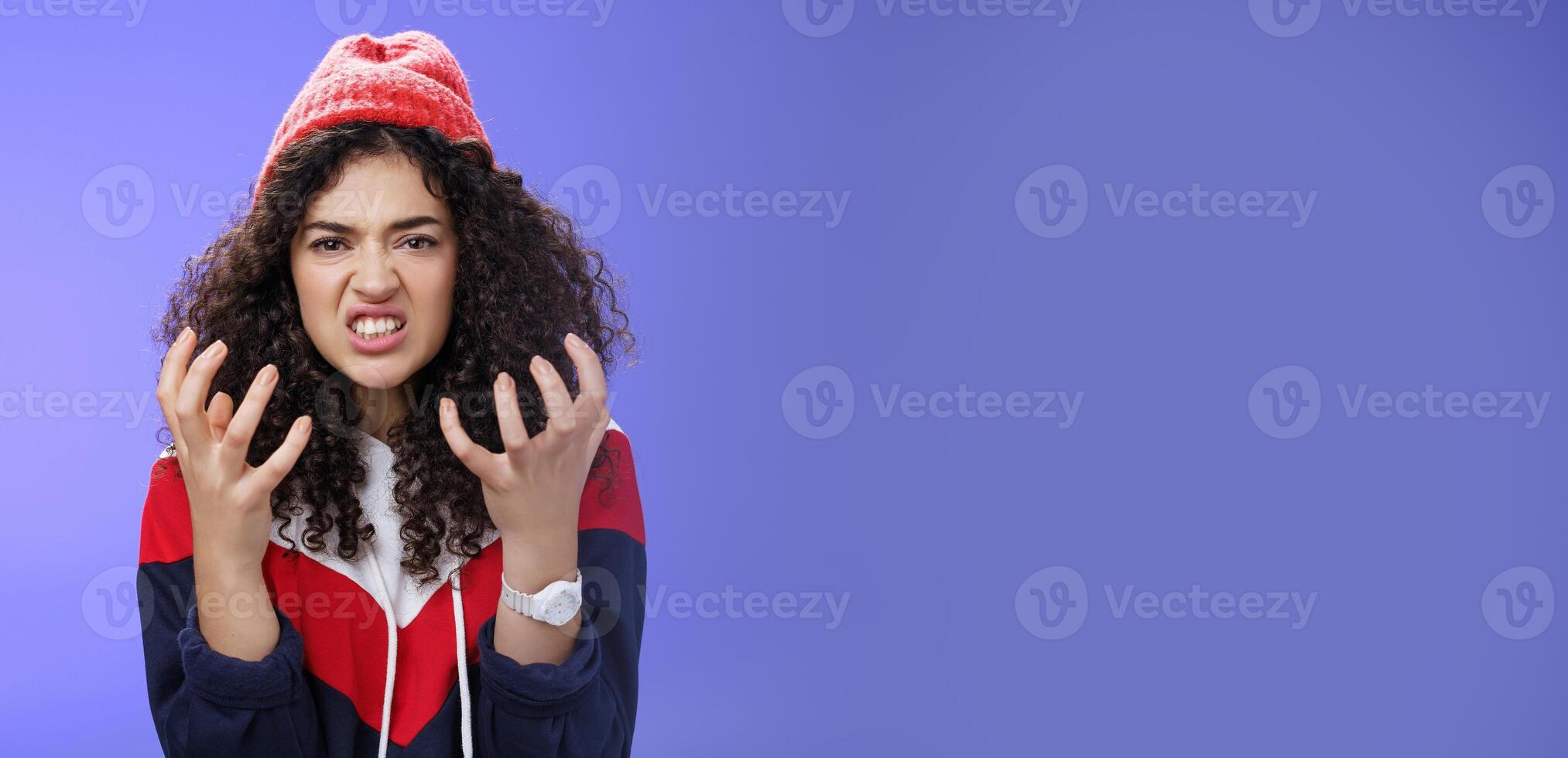 Pissed and annoyed stylish girl clenching hands in anger, grimacing squeezing teeth from annoyance and irritation, standing hateful and outraged feeling fury and hate posing over blue background photo