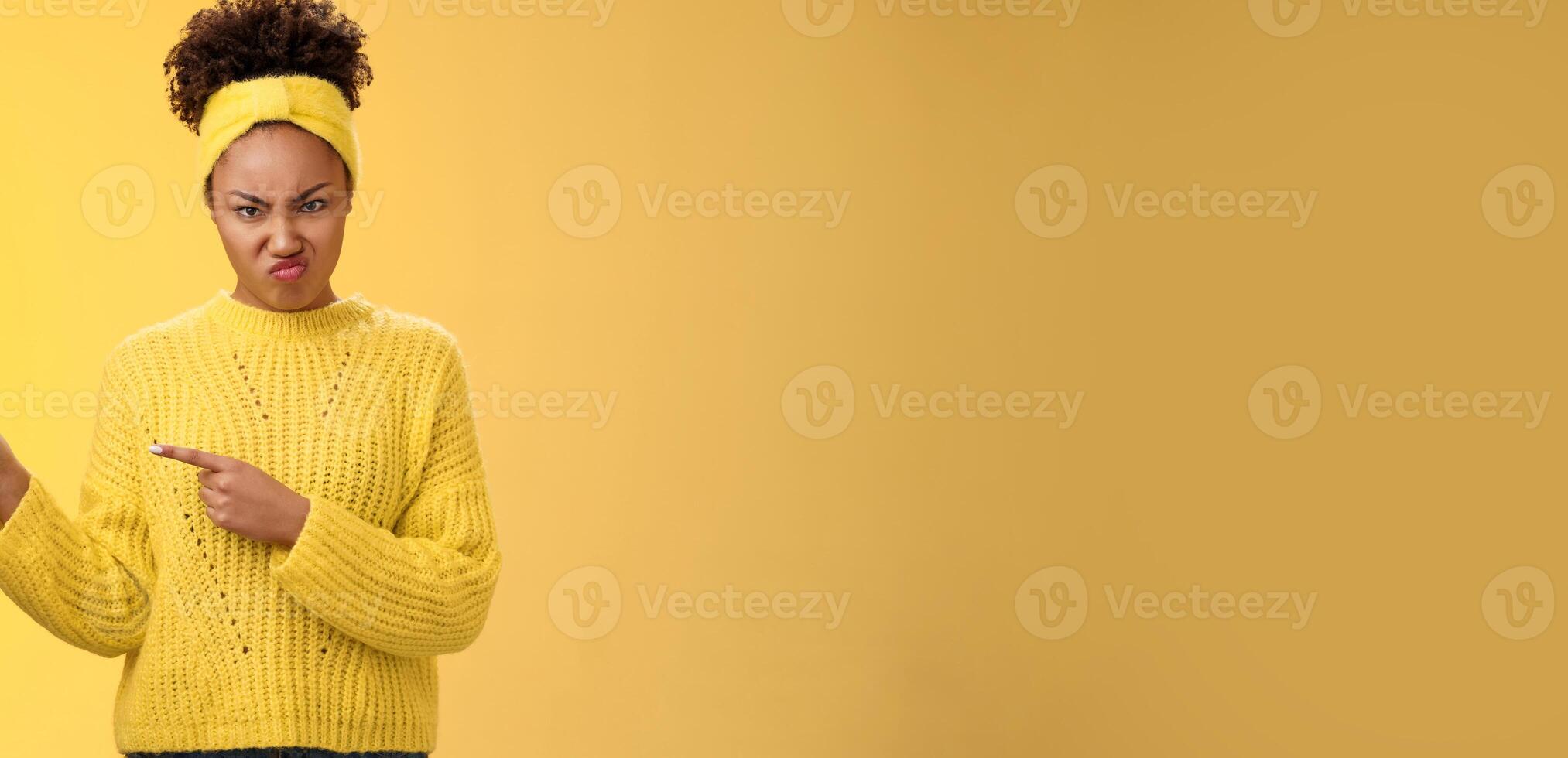 Arrogant peeky young girlfriend behave rude disrespectful frowning wrinkle nose disgust offence pointing left frowning dislike annoyance aversion, express disappointment, standing yellow background photo