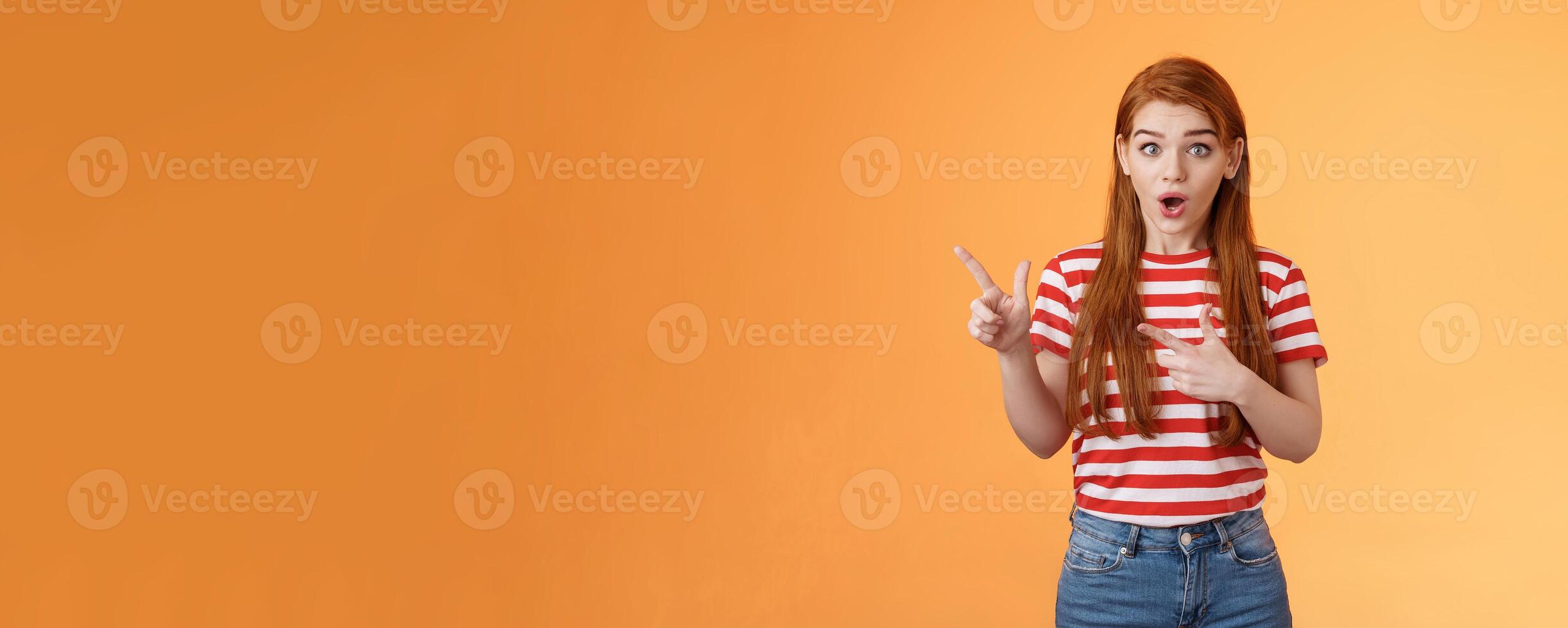 Wow awesome. Impressed excited beautiful redhead woman look astonished explain amazing news, stare camera thrilled talking about advertisement, pointing left upbeat impressed, orange background photo