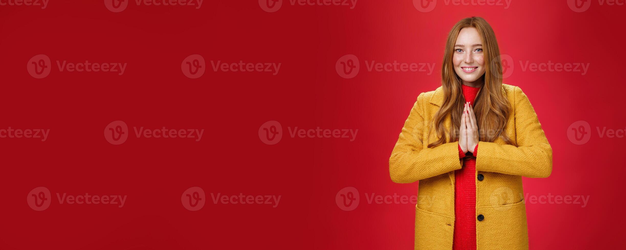 Girl welcomes us with buddhist namaste gesture pressing palms together over chest smiling friendly and delighted with carefree emotions holding hands in pray, posing happily over red background photo