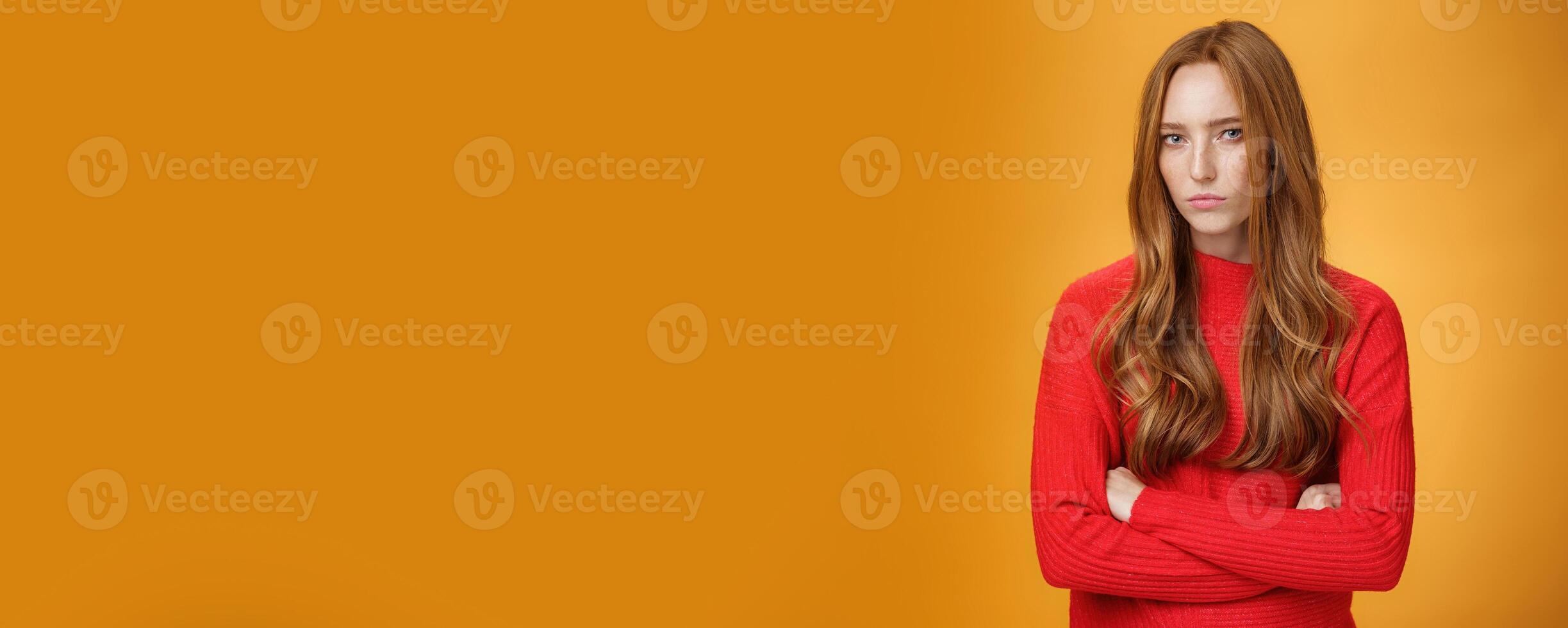 Suspicious intense and defensive ginger girl standing in passive-aggressive pose pouting and frowning looking with disbelief and disdain at camera, offended against orange background photo