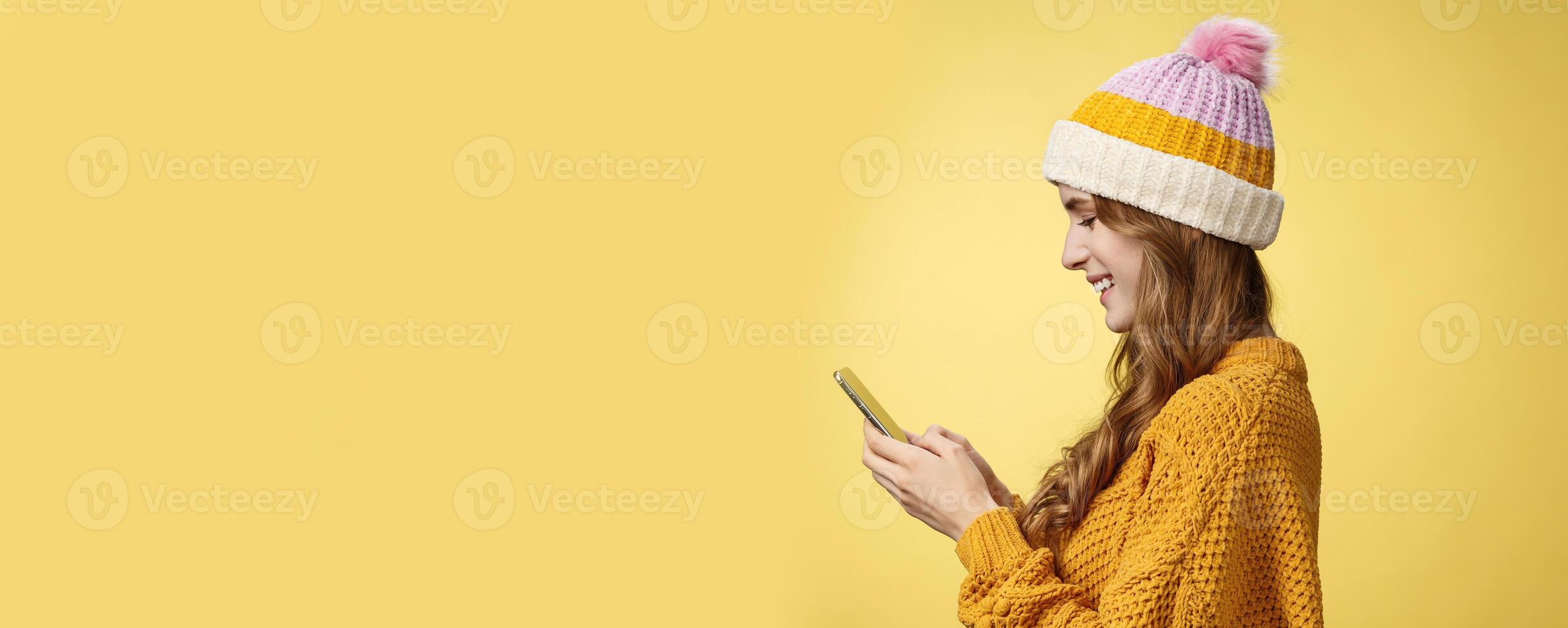 Profile shot charming outgoing relaxed young modern millennial girl texting smiling broadly holding smartphone looking display amused editing pic post online, blogger messaging followers photo
