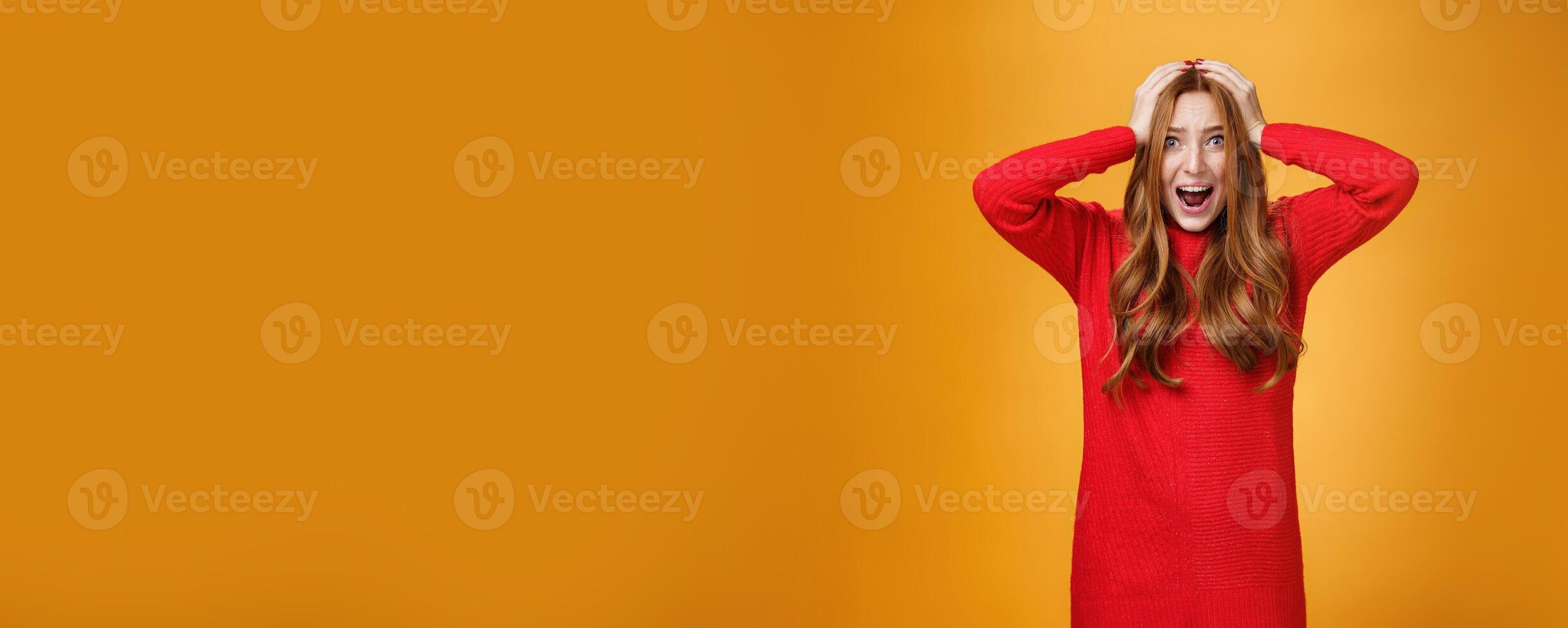 Girl goes insane from pressured panicking feeling tensed and troubles yelling from anxiety, worries being in difficult situation holding hands on head popping eyes, posing concerned over orange wall photo