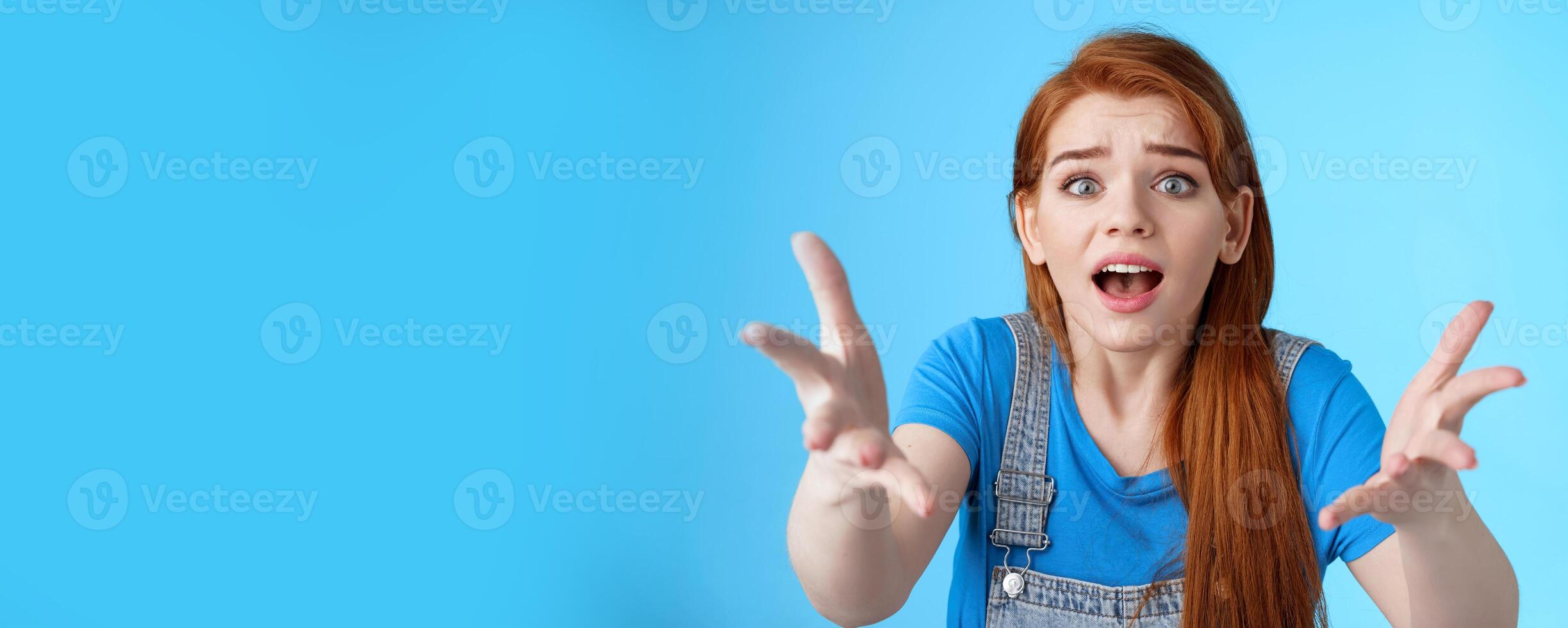 Close-up uneasy disappointed cute gloomy redhead girl, raise hands dismay full dibelief, frowning gasping upset, losing competition, receive bad results, stand blue background unhappy photo