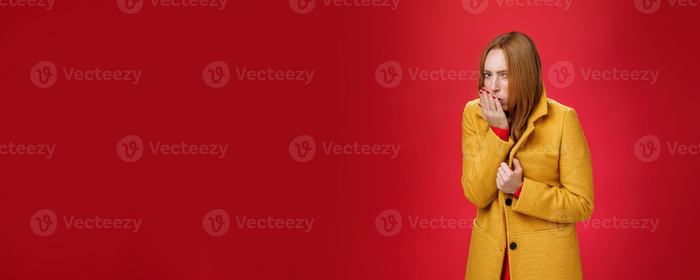 Girl getting cold, coughing and buttoning yelling light coat as freezing on chilly, windy weather looking displeased and ill at camera, feeling unwell catching flu over red background photo