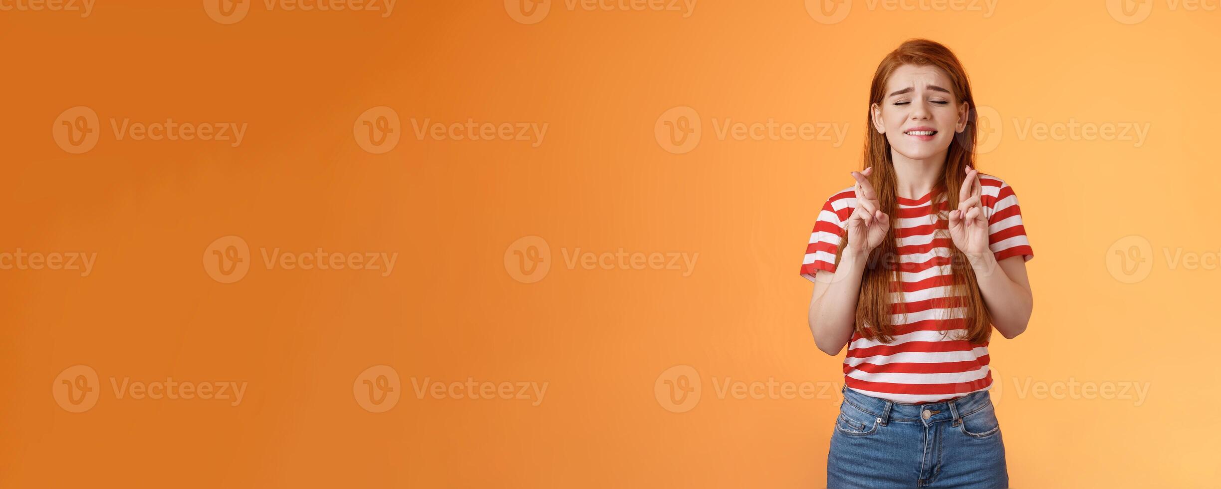 Hopeful cute redhead woman praying results be okay, faithfully cross fingers good luck, bite lip nervously believe she win, close eyes supplicating, plead lord dream come true, orange background photo