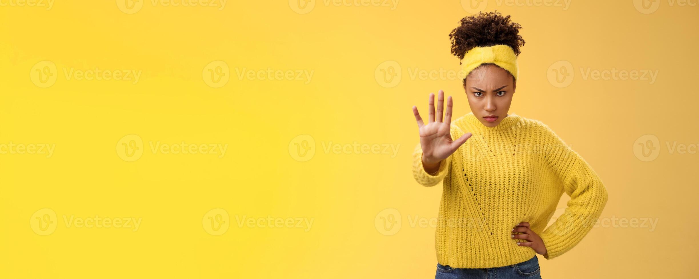 Brave serious-looking female african american femenist look from under forehead confident powerful pose raise palm stop enough not decline gesture forbid behave bad, standing yellow background photo