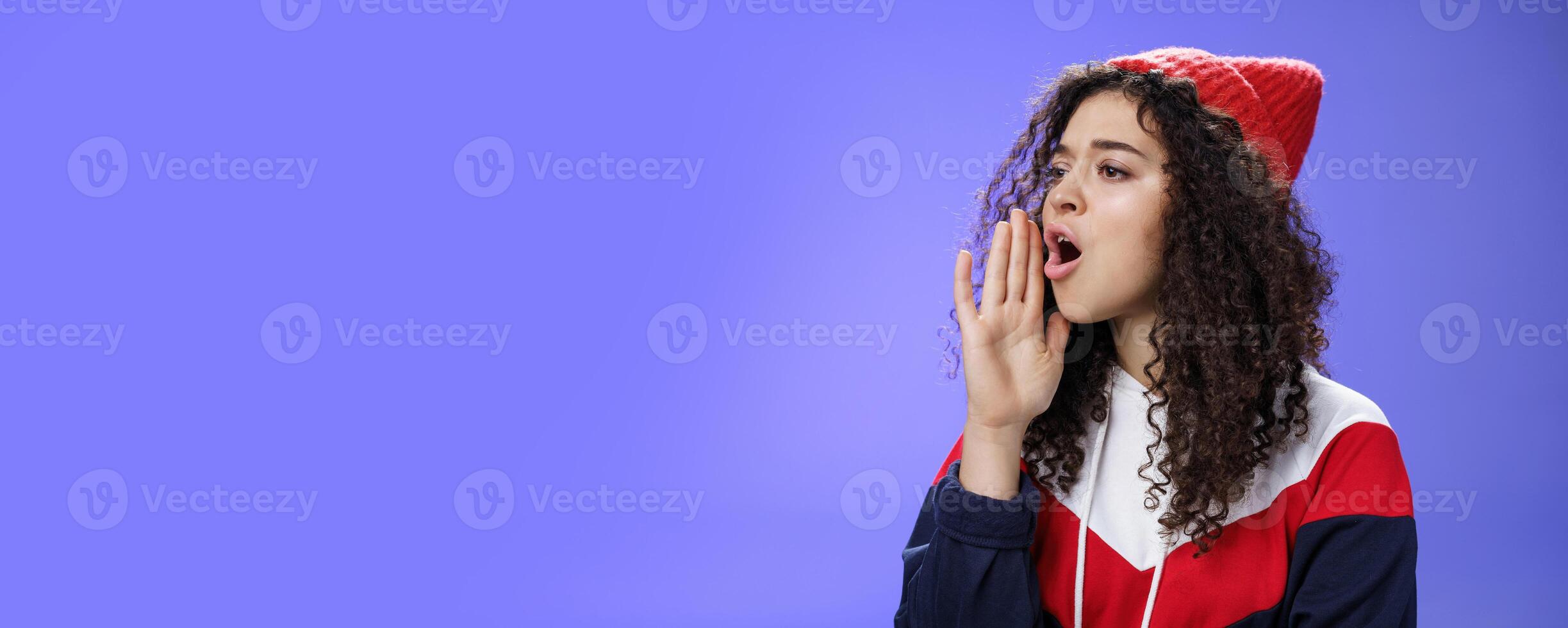Portrait of worried sister calling sibling outdoors open mouth looking left seriously and holding palm near lips as shouting name searching someone, posing concerned over blue background photo