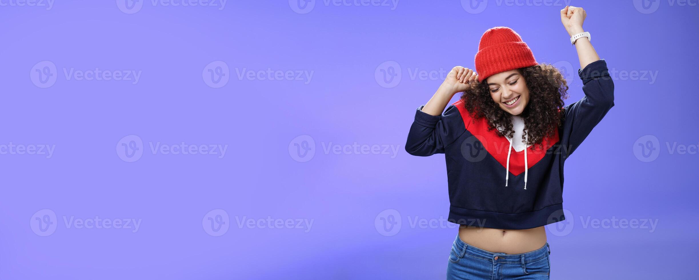 Girl celebrating favorite season in year. Portrait of carefree and joyful dancing woman with curly hair in cute red hat lifting hands in dance movements smiling enjoying music and holidays photo
