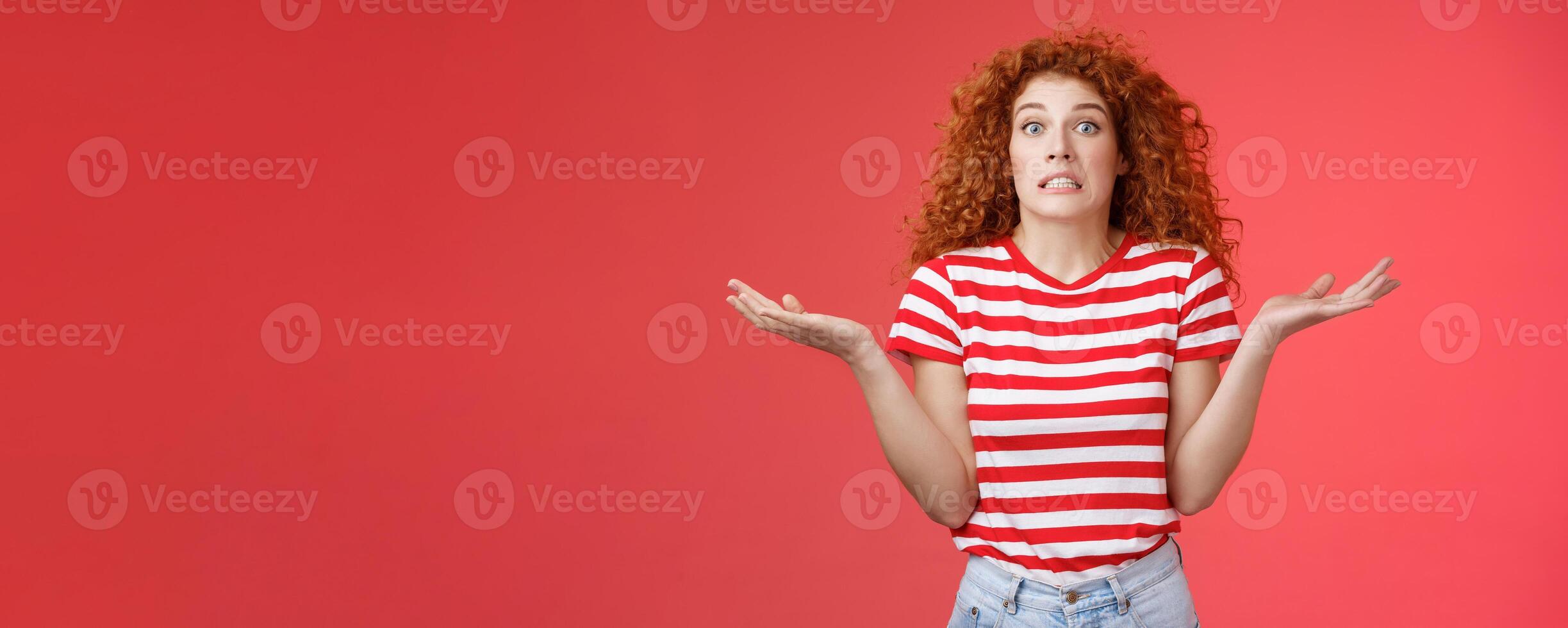 Yikes how should I know. Unaware worried awkward cute redhead curly girl clench teeth smirking uncertain panic cannot answer popping eyes confused shrugging hands spread sideways full disbelief photo