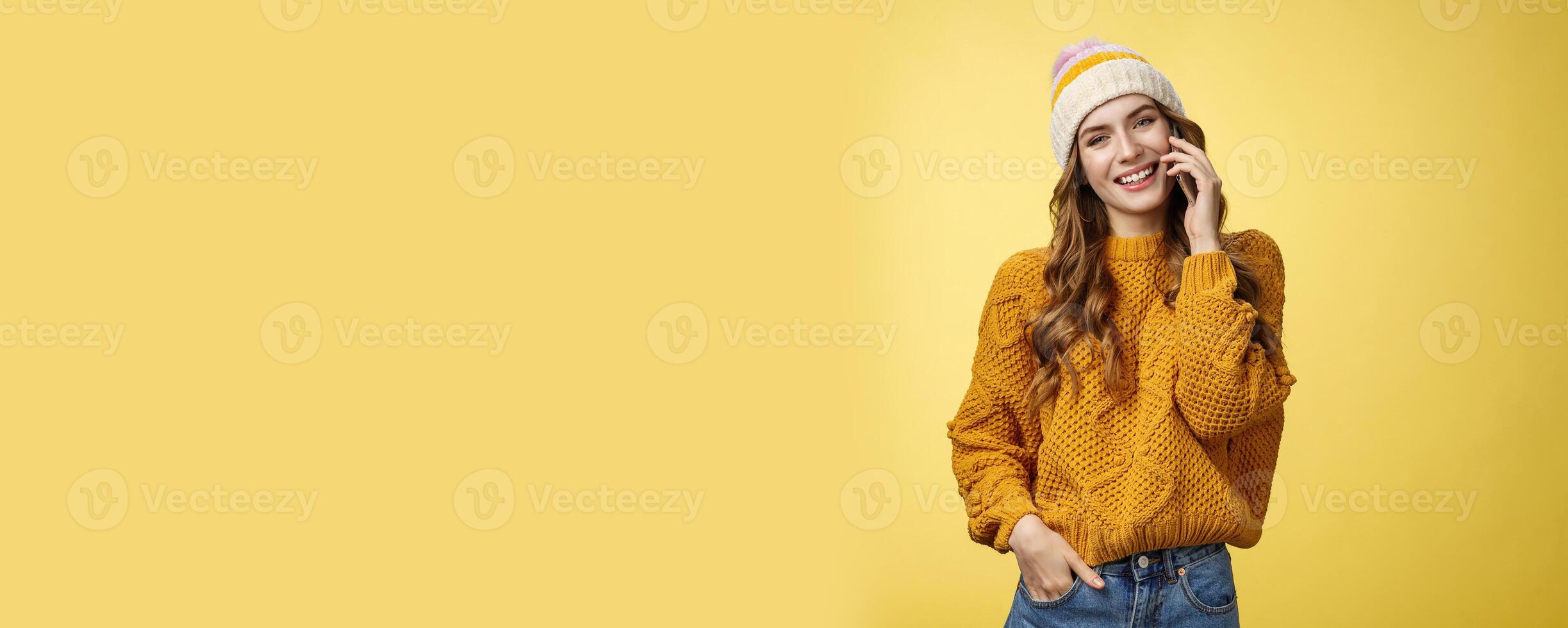 Charming stylish european woman wearing hat sweater tilting head flirty smiling talking smartphone calling boyfriend consulting friend via cellphone, standing happily casual pose yellow background photo