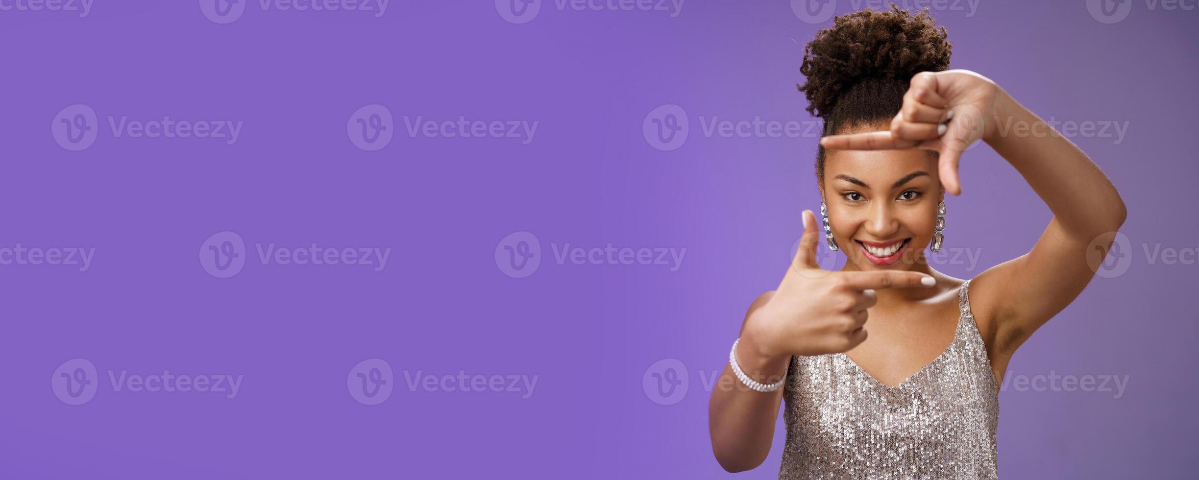 Creative good-looking african woman in silver glittering dress searching inspiration make finger frame look camera pleased smiling satisfied found perfect photo angle, standing blue background