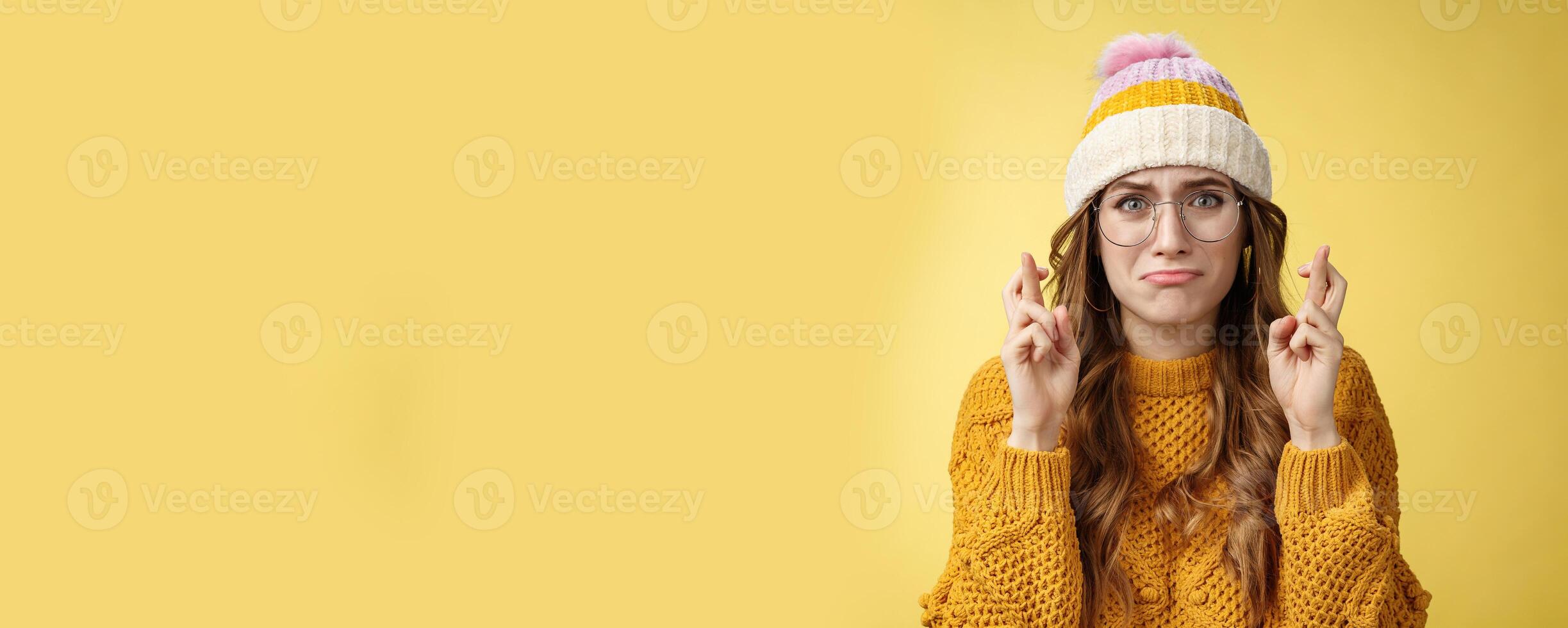Nervous insecure unconfident cute nerd girl university student wearing glasses sulking cry, whining worried cross fingers good luck praying dream come true standing intense yellow background photo