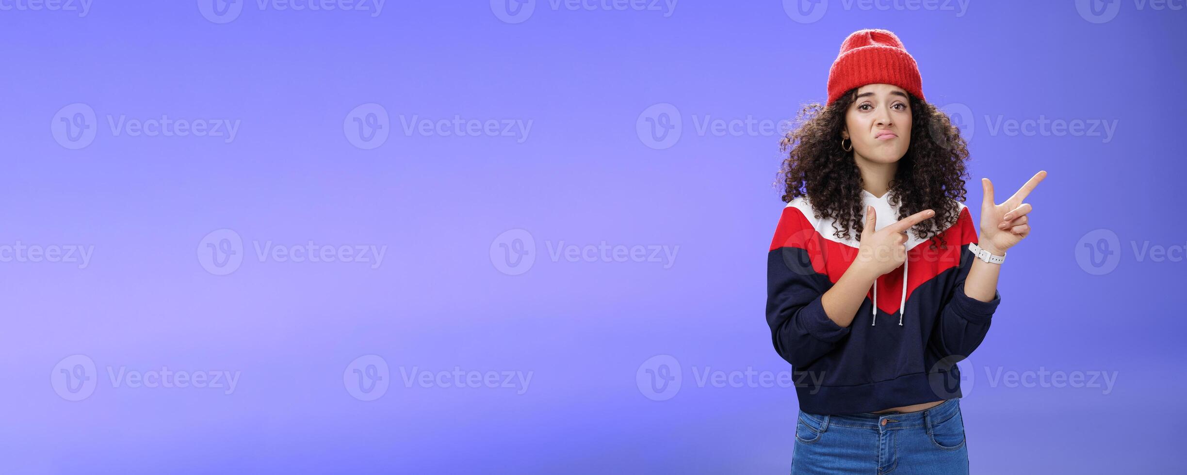 Girl with regret grimace and sorrow pointing at upper right corner jealous of guys playing outdoors asking friend join her pouting and frowning unhappy feeling upset against blue background photo