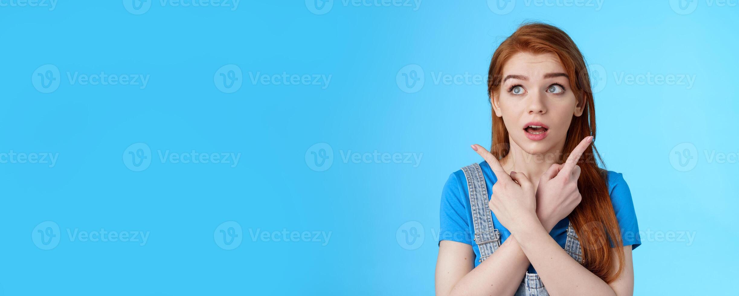 Uncertain cute redhead female making decision, cross arms body, pointing sideways upper left right corners, look aside hesitant, thinking, open mouth wondered, choosing products, blue background photo
