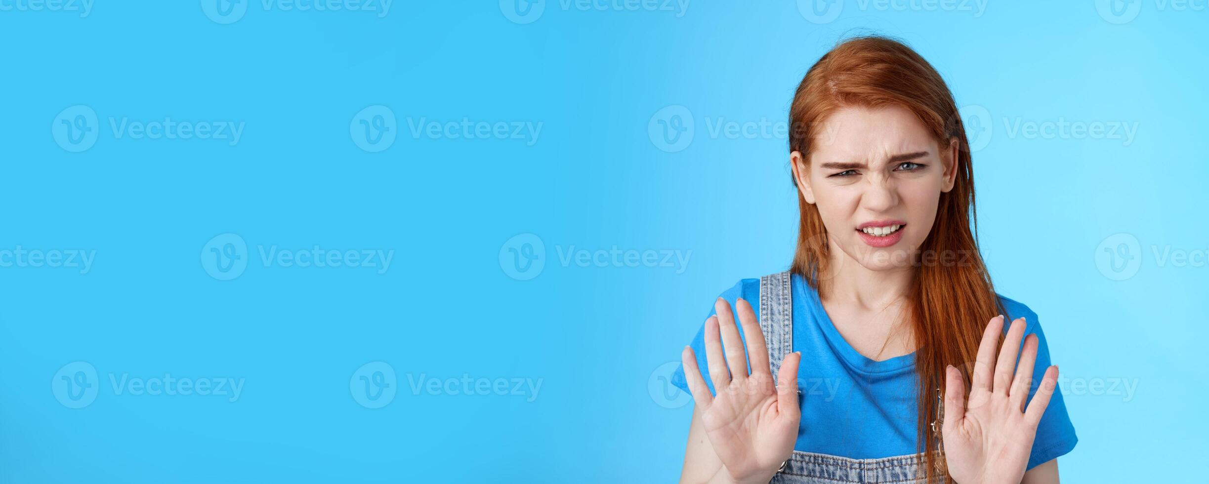 Close-up uninterested displeased ignorant picky redhead girlfriend, frowning make disgusted grimace raise hands block stop gesture, refuse, waving arms no rejection sign, stand blue background photo