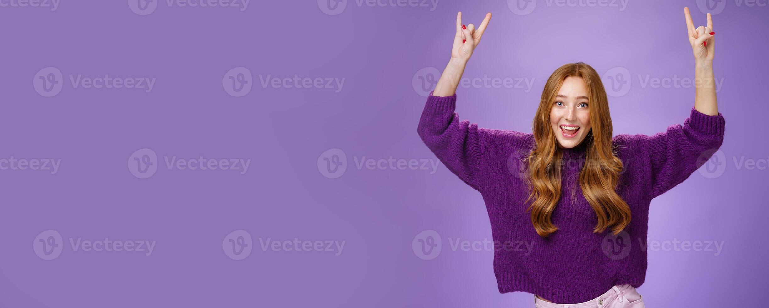 Girl feeling excited finally receiving tickets for favorite band show, raising hands with rock-n-roll gesture yelling yeah and smiling broadly, happy and thrilled against purple background photo