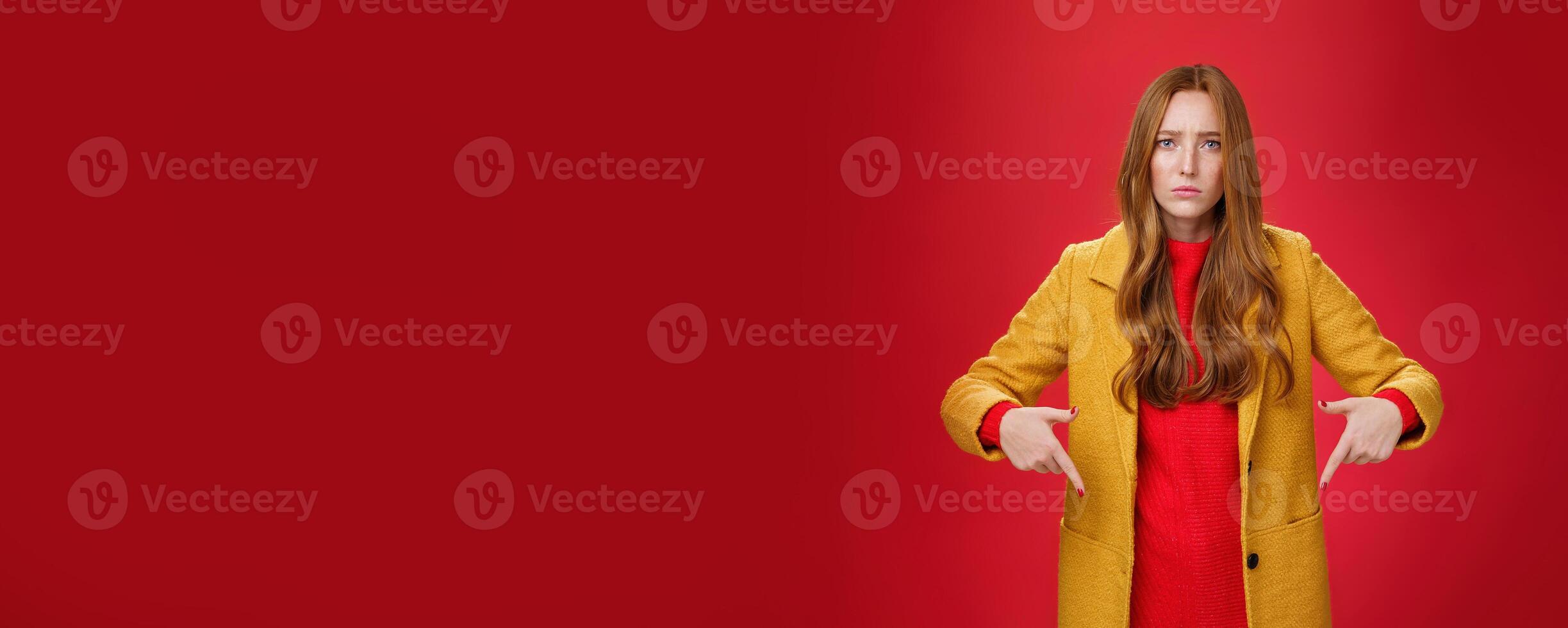 Portrait of sad and displeased moody girlfriend asking opinion with concerned upset expression pointing down looking focused and serious with unhappy face at camera over red background photo