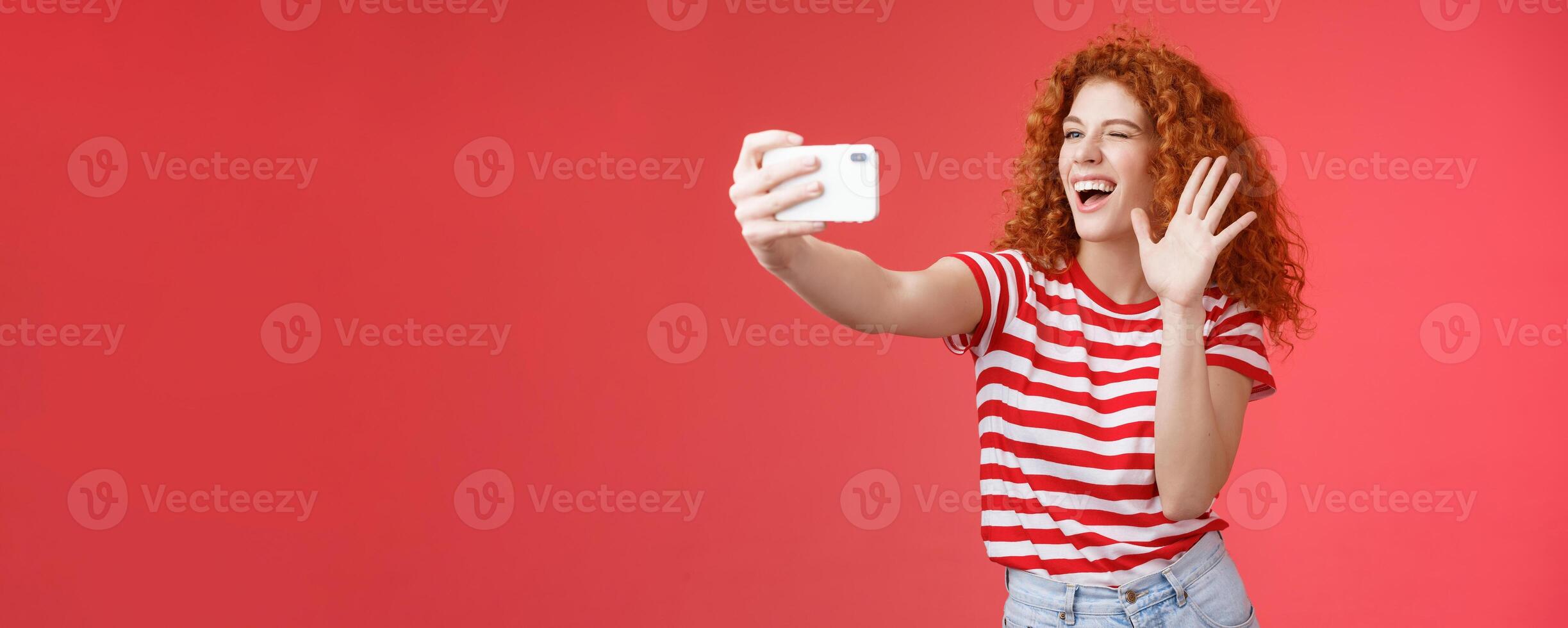 Cheerful friendly energized good-looking redhead curly-haired female send hello waving palm smiling broadly blogger record life stream talking fans grinning taking selfie summer holiday trip photo