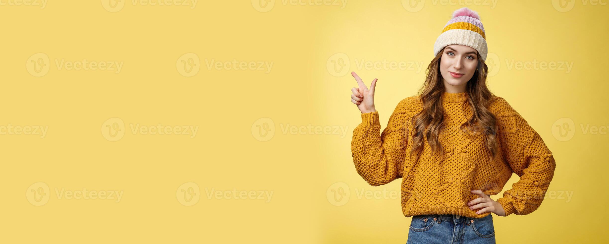 Confident good-looking young female friend telling you buy product immidietely pointing upper left corner smiling hold hand waist self-assured, employee help client pick best merch, yellow background photo