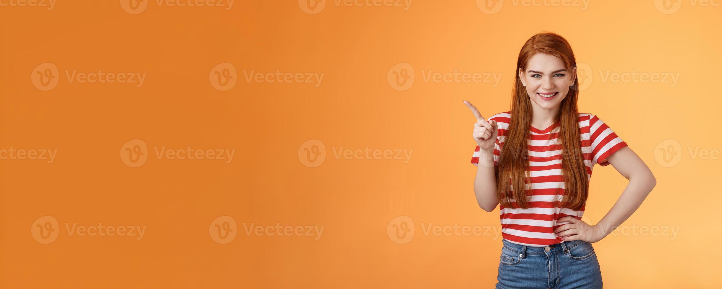 Cheerful sly redhead girlfriend have something interesting on mind, squinting cunning joyful smile, hold hand waist confident pose, pointing upper left corner give recommendation, orange background photo