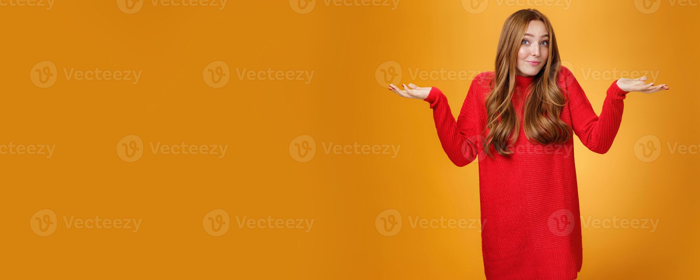What do I know. Portrait of confused clueless tender and gentle redhead woman in red sweater shrugging with hands raised near shoulders turning away questioned and unaware, not knowing photo