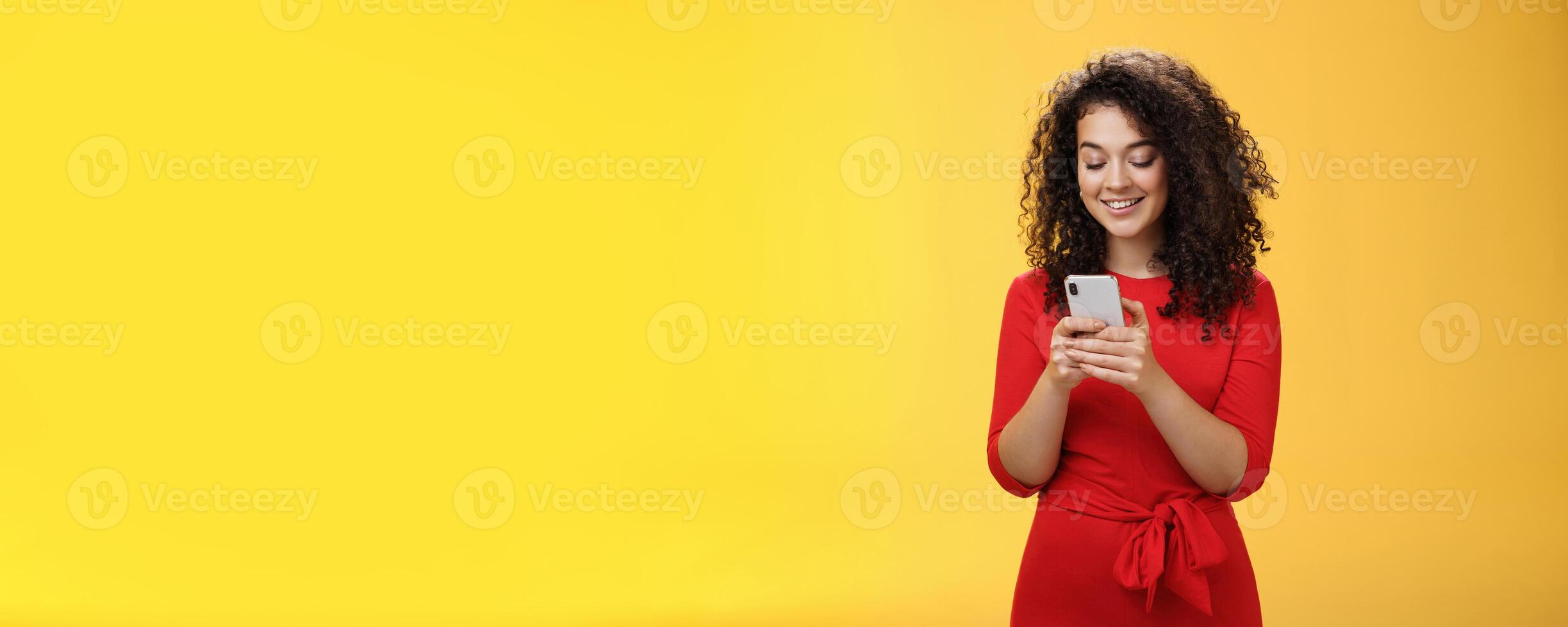 Gil sending message spread news across social network having party inviting friends via smartphone holding mobile phone in hands smiling broadly at device screen as posing over yellow background photo
