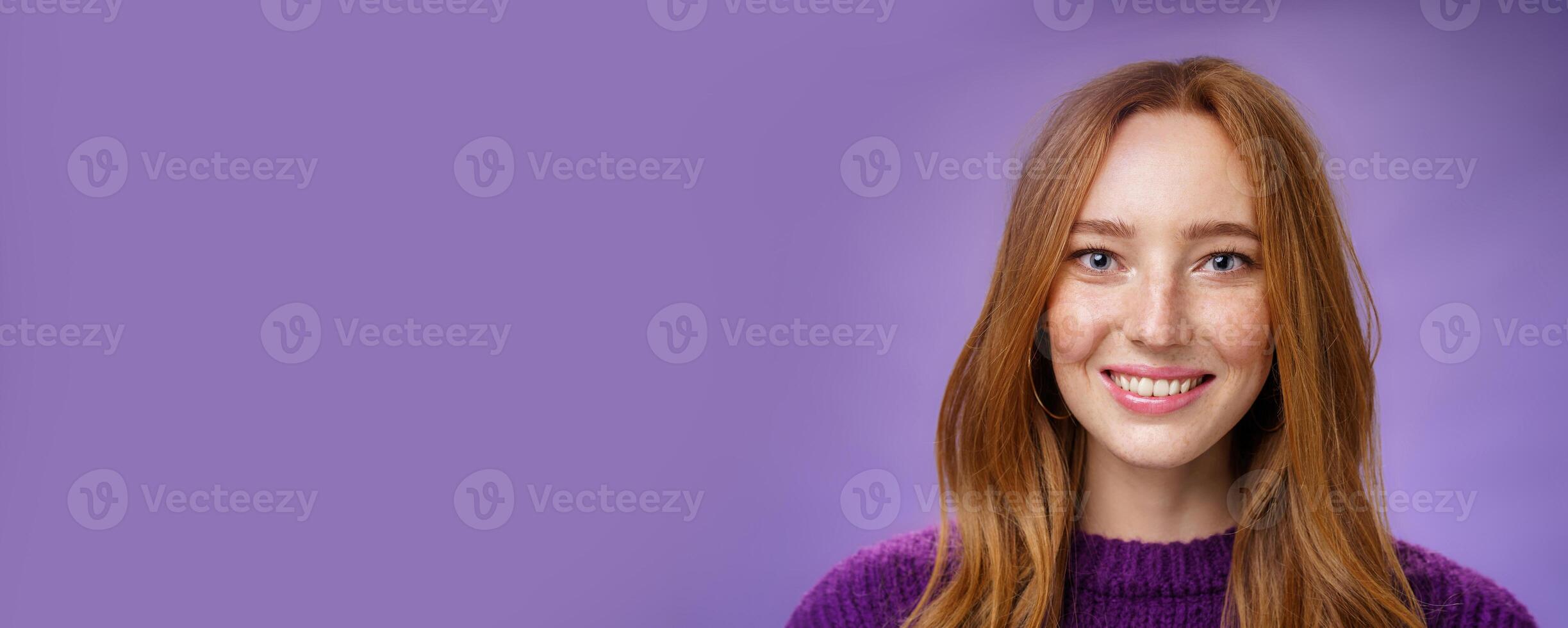 Headshot of charming attractive and happy young redhead woman with freckles and bright white smile, grinning satisfied at camera as posing over purple background friendly and delighted photo