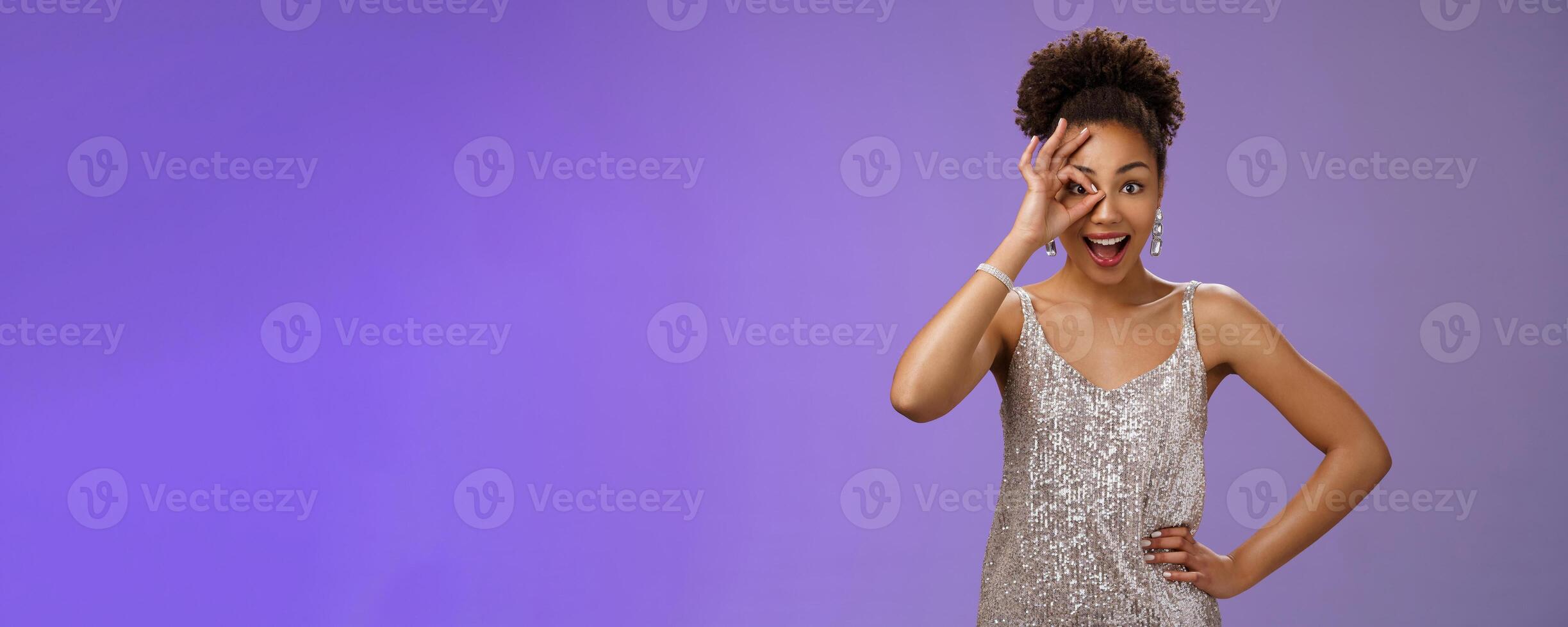 Good-looking charismatic enthusiastic flirty african-american woman in silver evening dress hold hand waist joyfully smiling open mouth impressed look through okay ok gesture amused photo