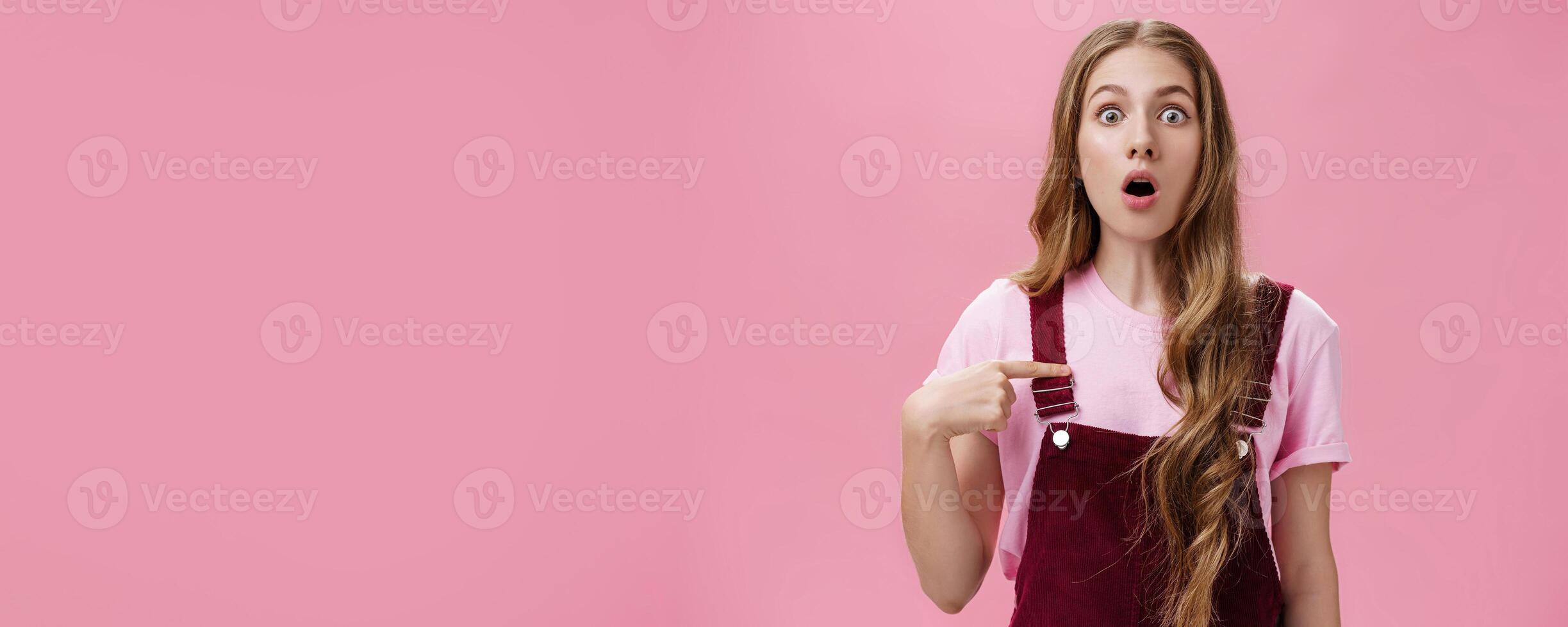 Shocked uncertain and confused charming young woman with tattoos and long natural wavy hair dropping jaw gasping and popping eyes from surprise pointing at herself with unsure expression photo