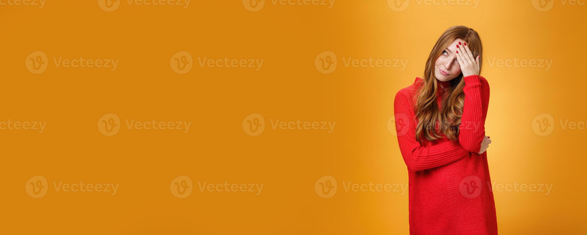Annoyed and pissed embarrassed woman hiding behind hand making facepalm gesture looking away with irritated humiliated gesture, standing fed up and intense against orange background photo