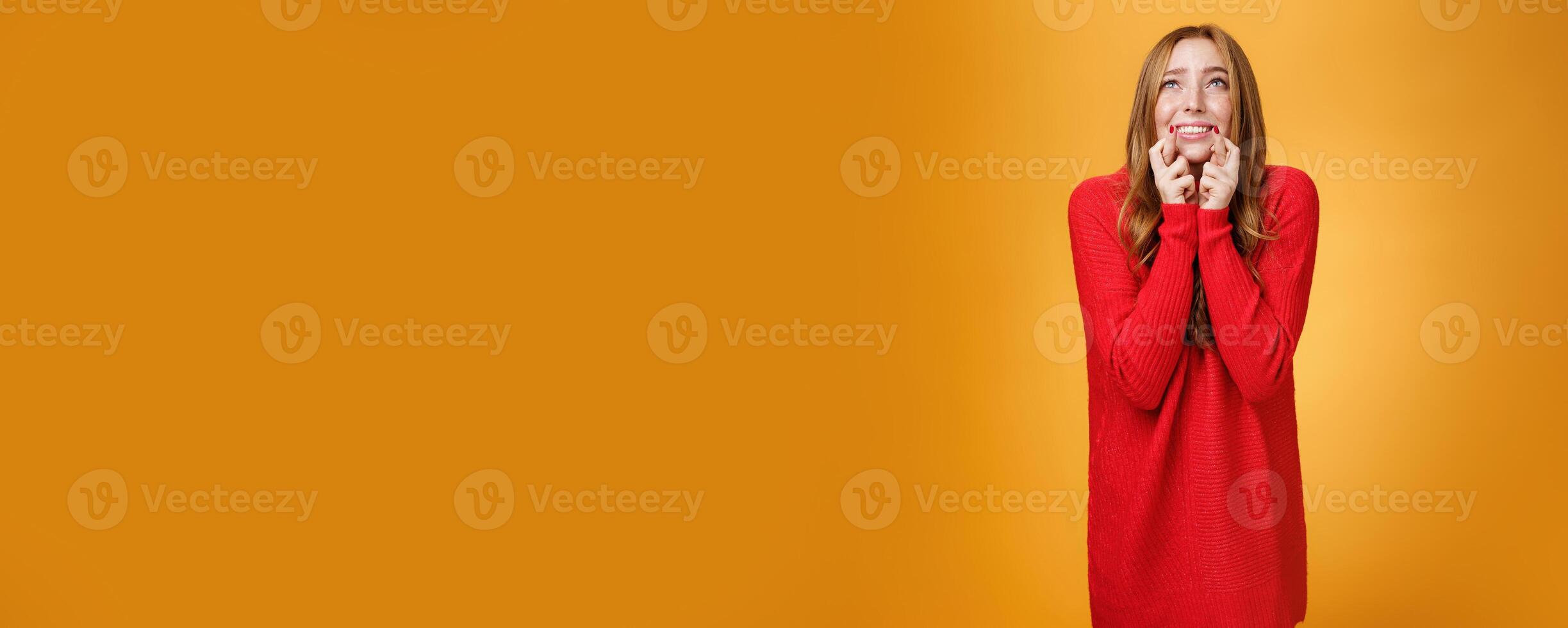Portrait of excited and worried young redhead female in 20s stooping standing in begging pose crossing finger for good luck looking at sky as praying god and asking help with wish come true photo