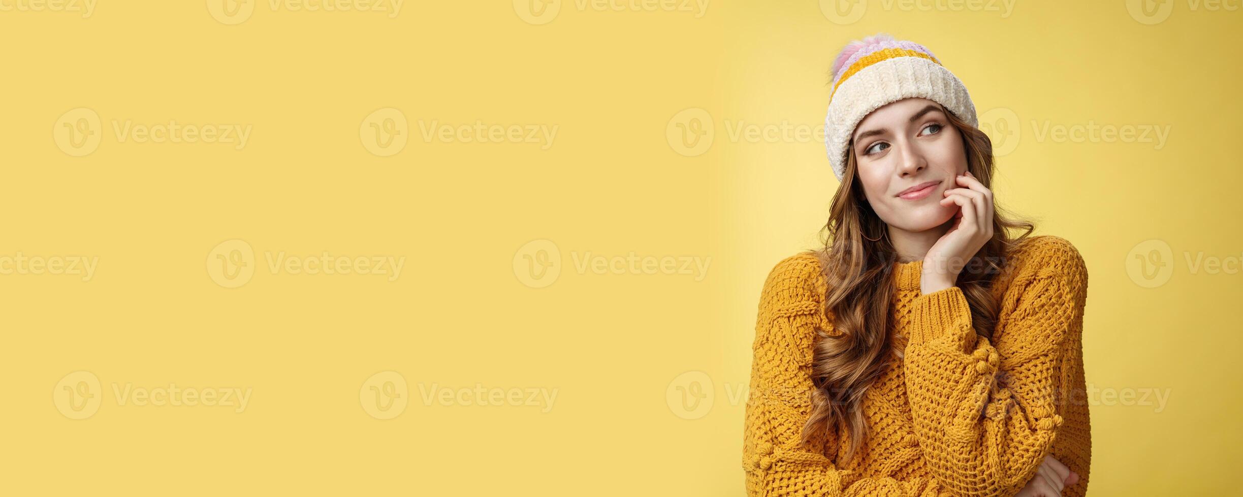 Dreamy creative charming girlfriend wearing warm hat sweater gazing right thoughtful imaging romantic date smiling happily picturing recalling lovely memories, standing delighted yellow background photo
