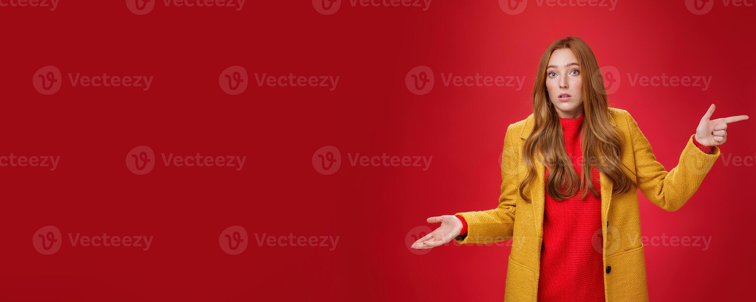 Woman missed client posing confused and unaware how happened shrugging making clueless gesture with palm as pointing right and looking questioned and uncertain at camera over red background photo
