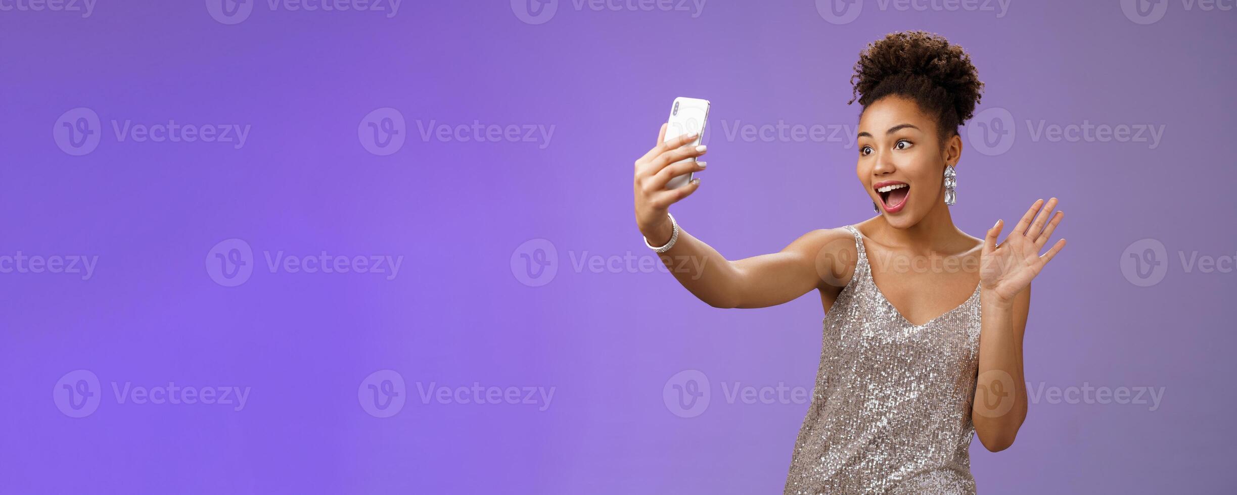 Friendly stylish confident african-american woman in silver glittering dress waving raised palm hello hi gesture record smartphone greeting internet followers blogging during party photo