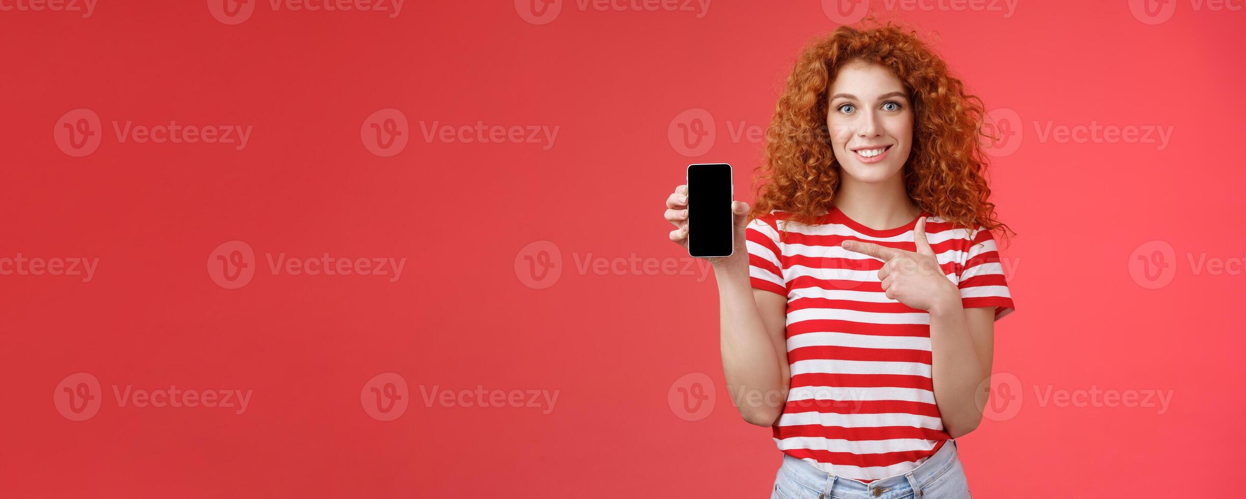 How about this app. Redhead curly friendly cute girl help friend find oufit online store hold smartphone pointing phone screen smiling broadly recommend social media photo filter, red background