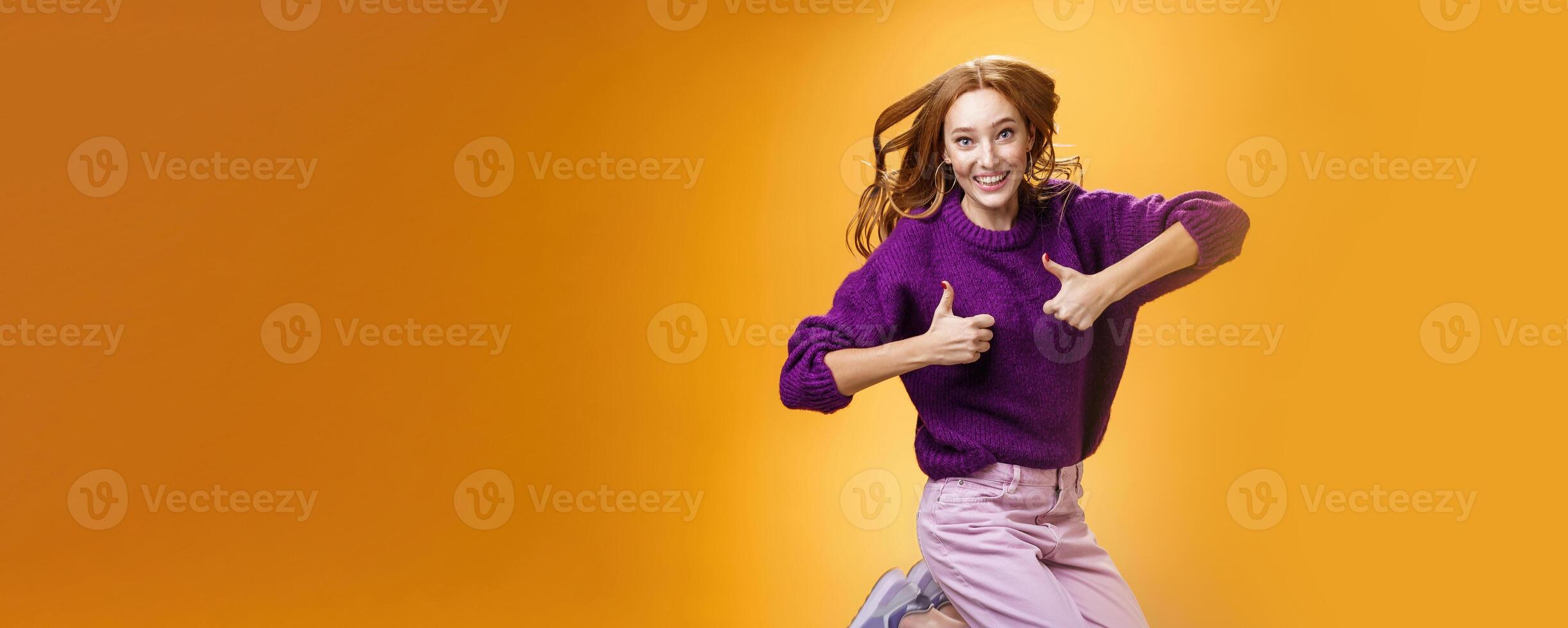 Optimistic and cheerful woman liking promotion lifting thumbs up and jumping from excitement and delighted, having fun recommending good idea smiling thrilled and enthusiastic over orange background photo