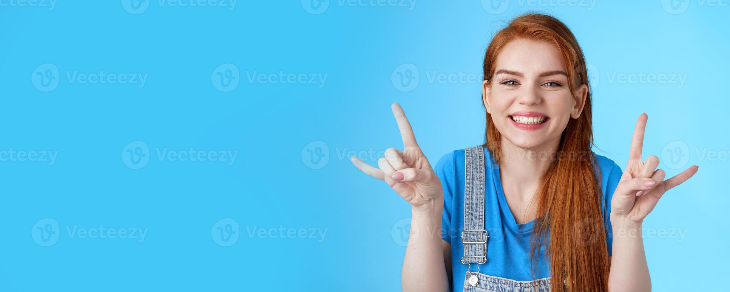 Close-up cheerful lucky joyful redhead woman having fun, enjoying summertime, show rock-n-roll gesture attend awesome party concert, make heavy-metal sign and smiling blue background photo