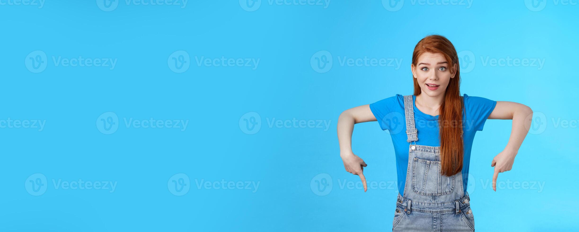 Curious tender lovely ginger caucasian girl, pointing down questioned, check out interesting promo, point bottom down copy space, look camera intrigued, suggest good product online shop link photo