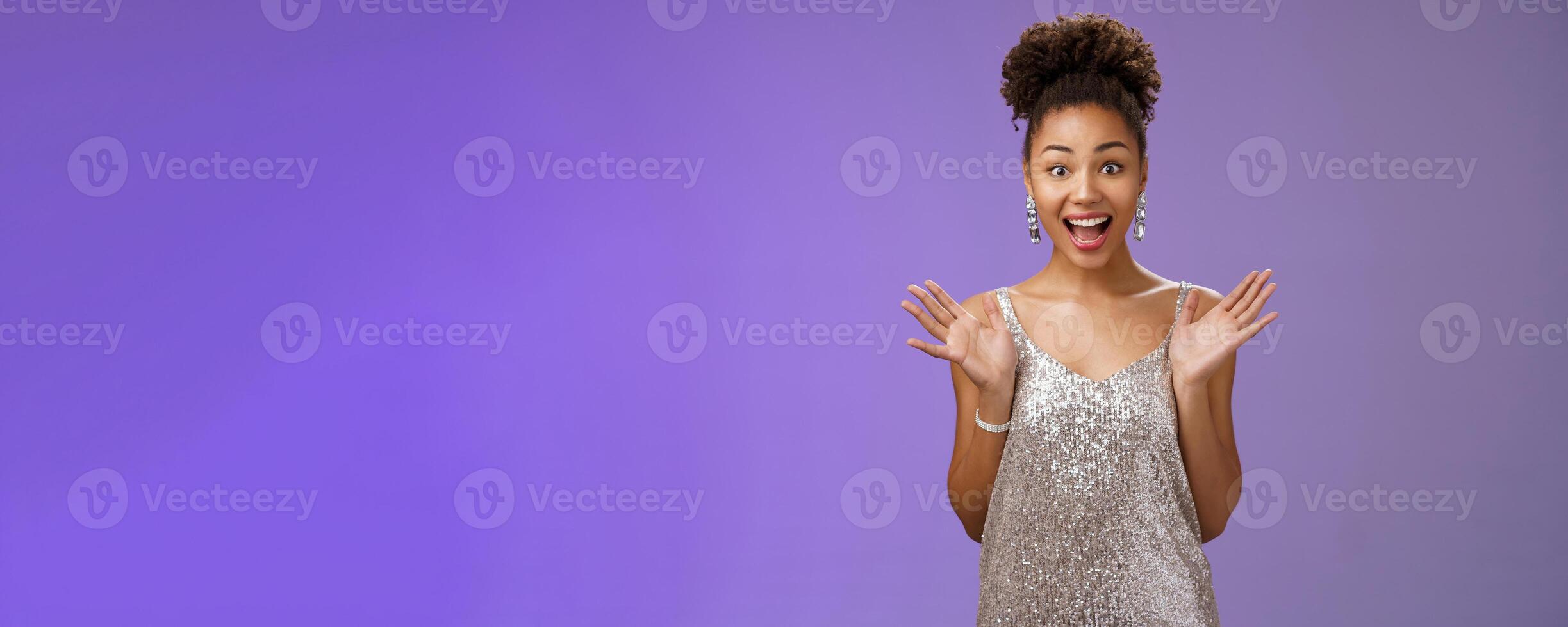 Surprised amused excited african-american woman in glittering shiny silver dress raise hands astonished pleased delighted meeting friend party smiling thrilled standing blue background amazed photo
