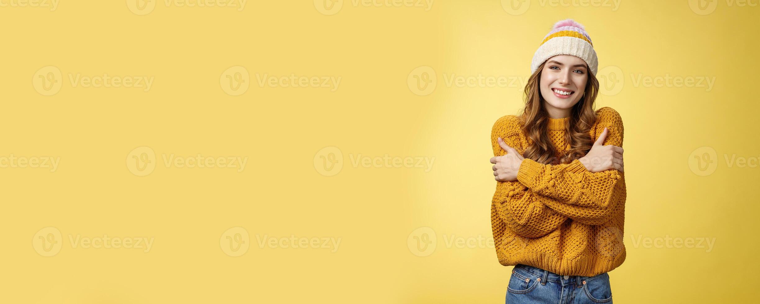 Getting cold bring jacket. Portrait charming tender feminine cute girlfriend embacing herself cuddling smiling warm gaze freezing outside standing knitted sweater hat, yellow background photo